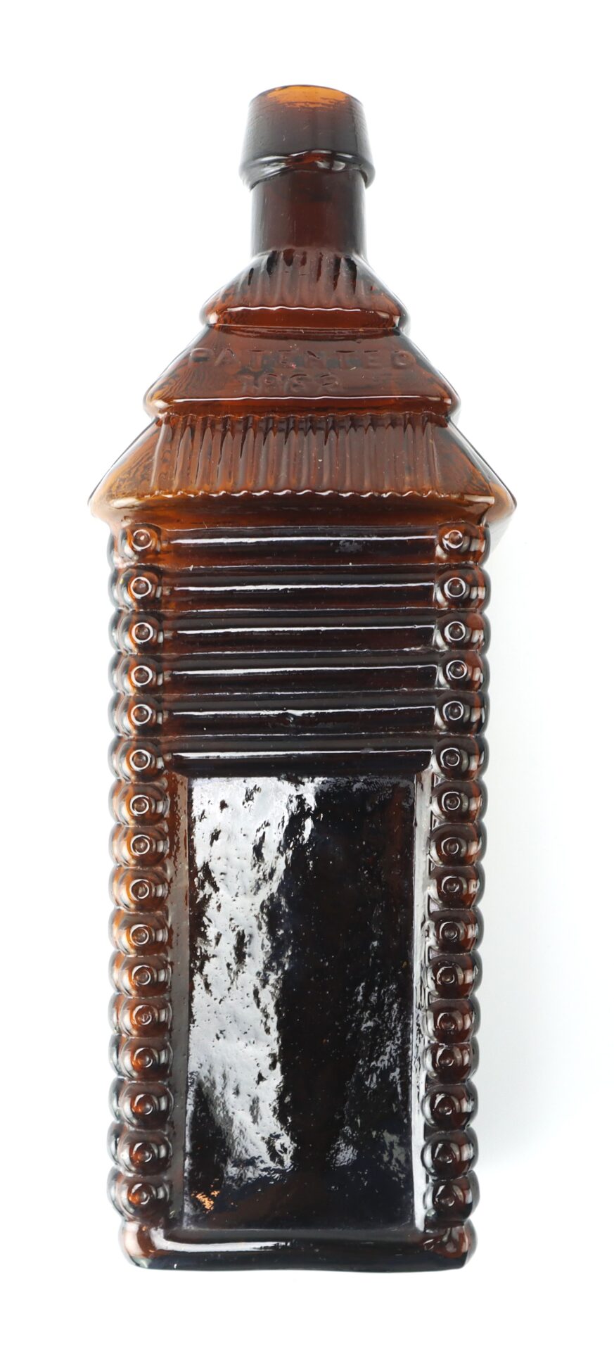 A brown glass bottle shaped like a log cabin with embossed log details and a rectangular label area, isolated on a white background.