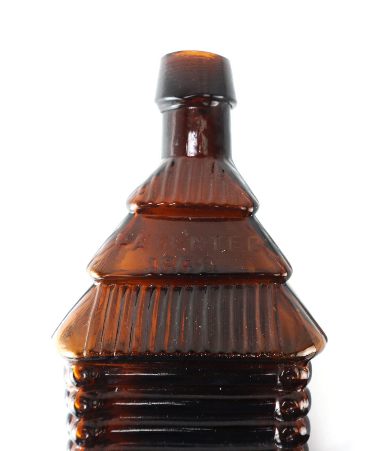 Amber glass bottle shaped like a log cabin with ridged detailing and the embossed text "Patented 1860" on the front.