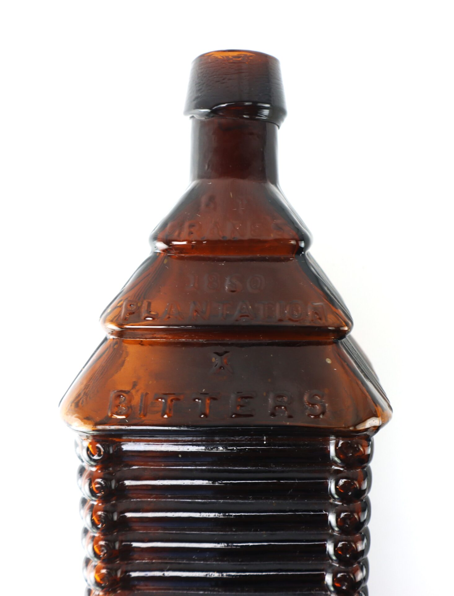 Amber glass bottle shaped like a log cabin with embossed text reading "1860 PLANTATION BITTERS" on the front, photographed against a white background.