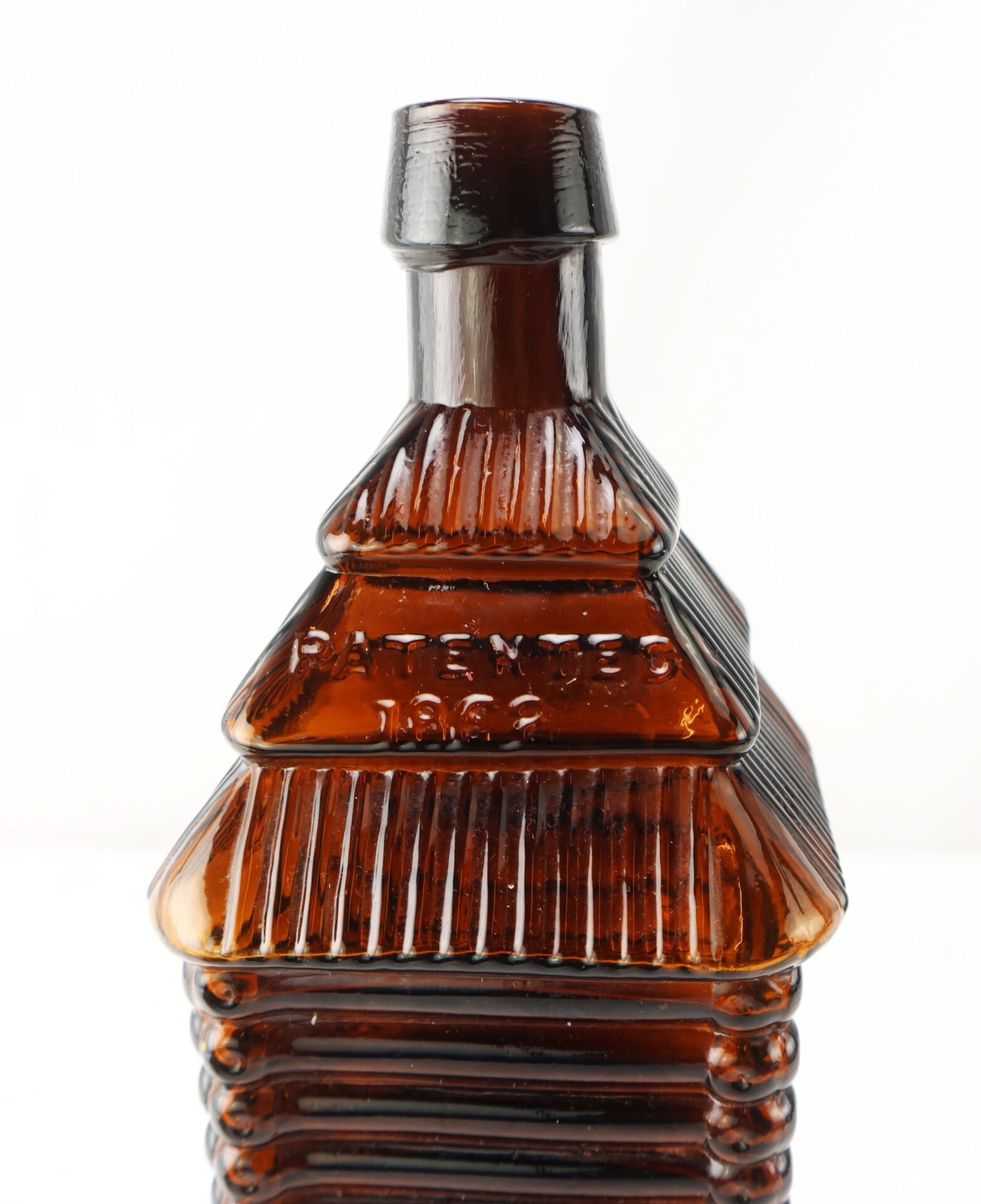 Brown glass bottle shaped like a log cabin with embossed text reading "PATENTED 1862" on the front, photographed against a plain white background.