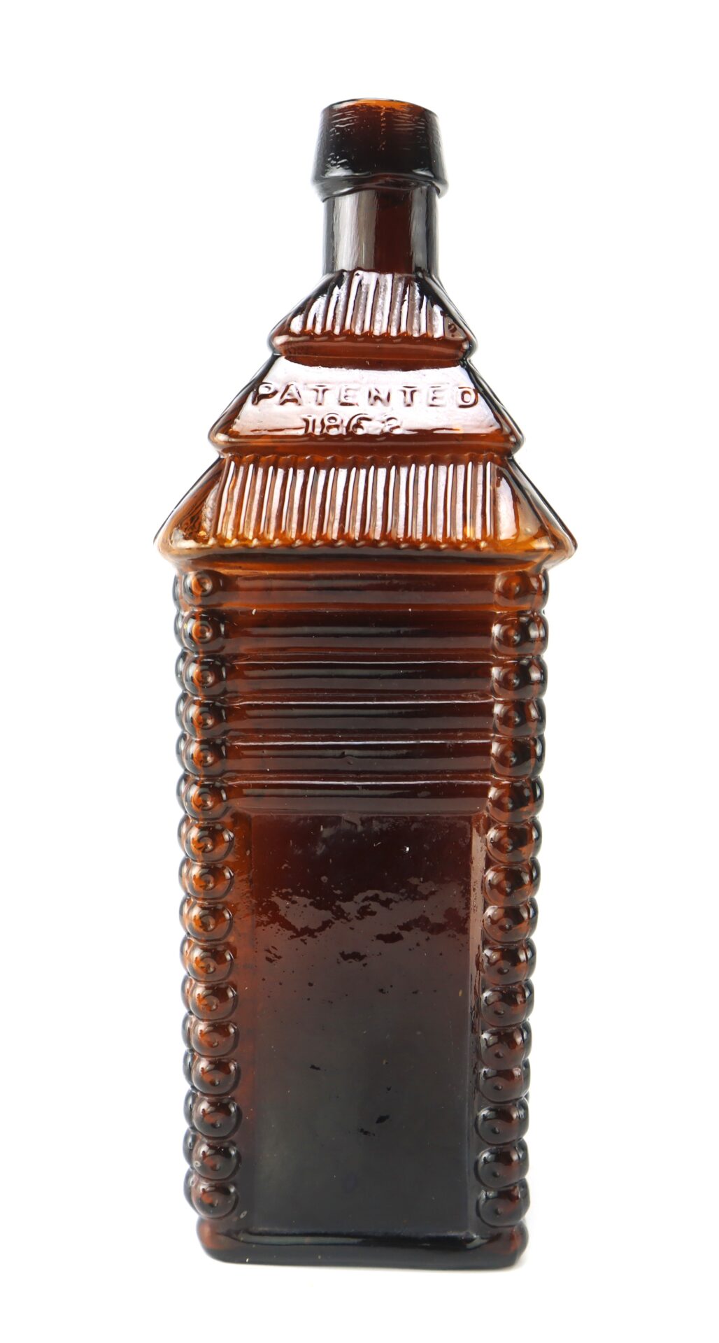Brown glass bottle shaped like a log cabin, with embossed lines and the word "PATENTED" visible near the top.