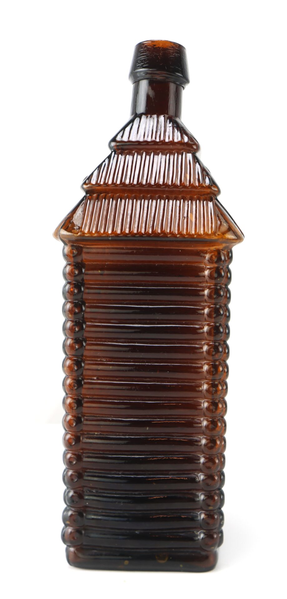 Brown glass bottle shaped like a log cabin with a textured roof and horizontal lines along the body, photographed on a white background.