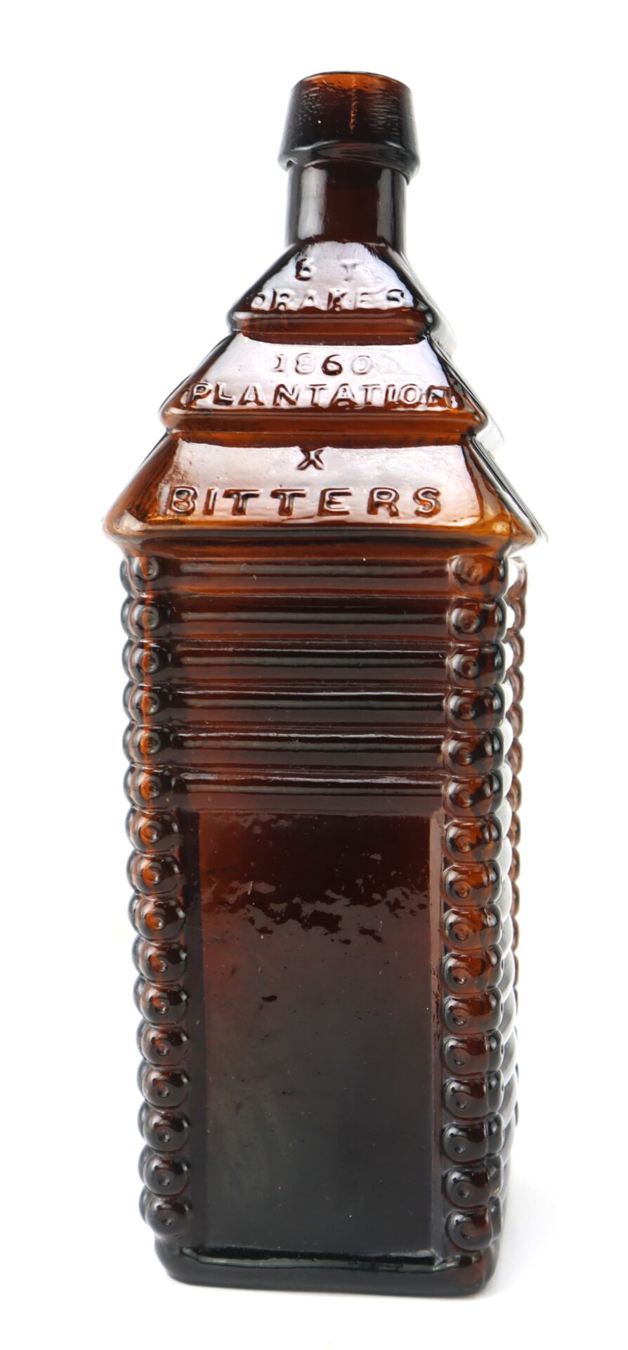 Amber glass bottle shaped like a small cabin, embossed with "1860 Plantation Bitters" on the front, with ridged and textured sides.