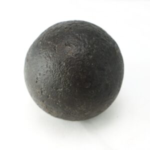 A single round, rough-textured, dark metal cannonball resting on a white surface.