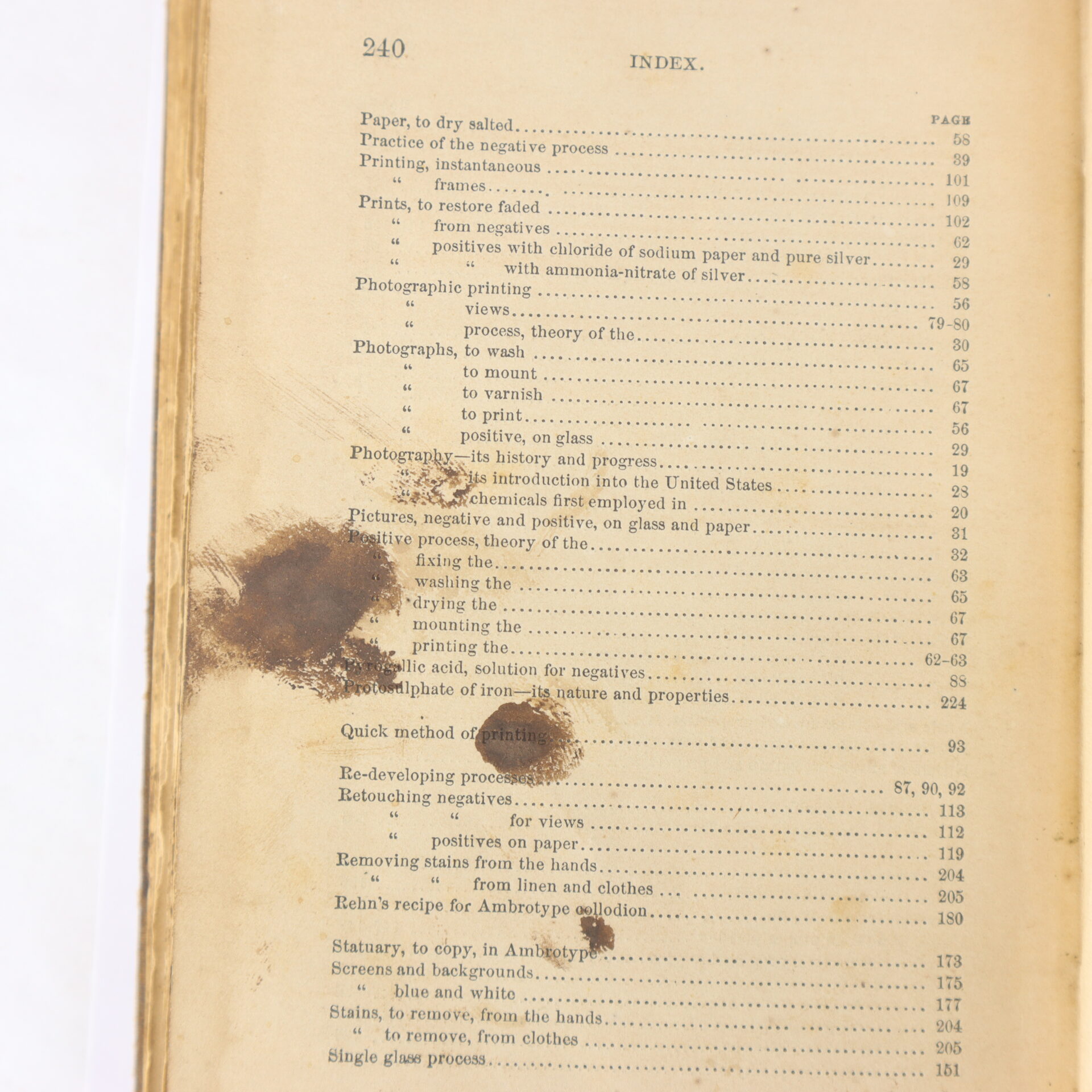 A stained index page from an old photography book, listing topics such as printing, positives, negatives, and various photographic processes.
