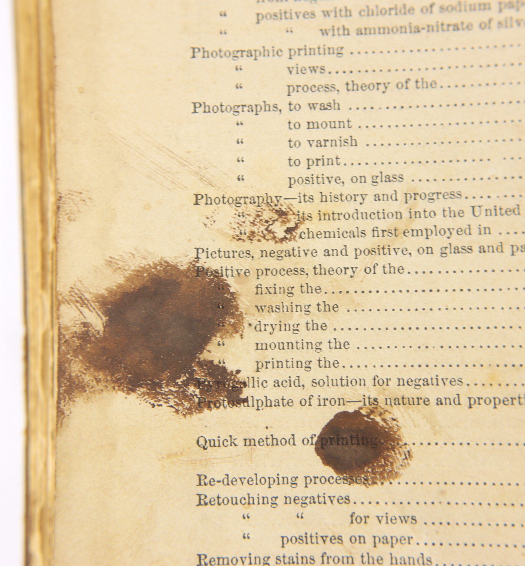 A close-up of a yellowed, stained book page with smudges and visible printed text discussing photographic processes.