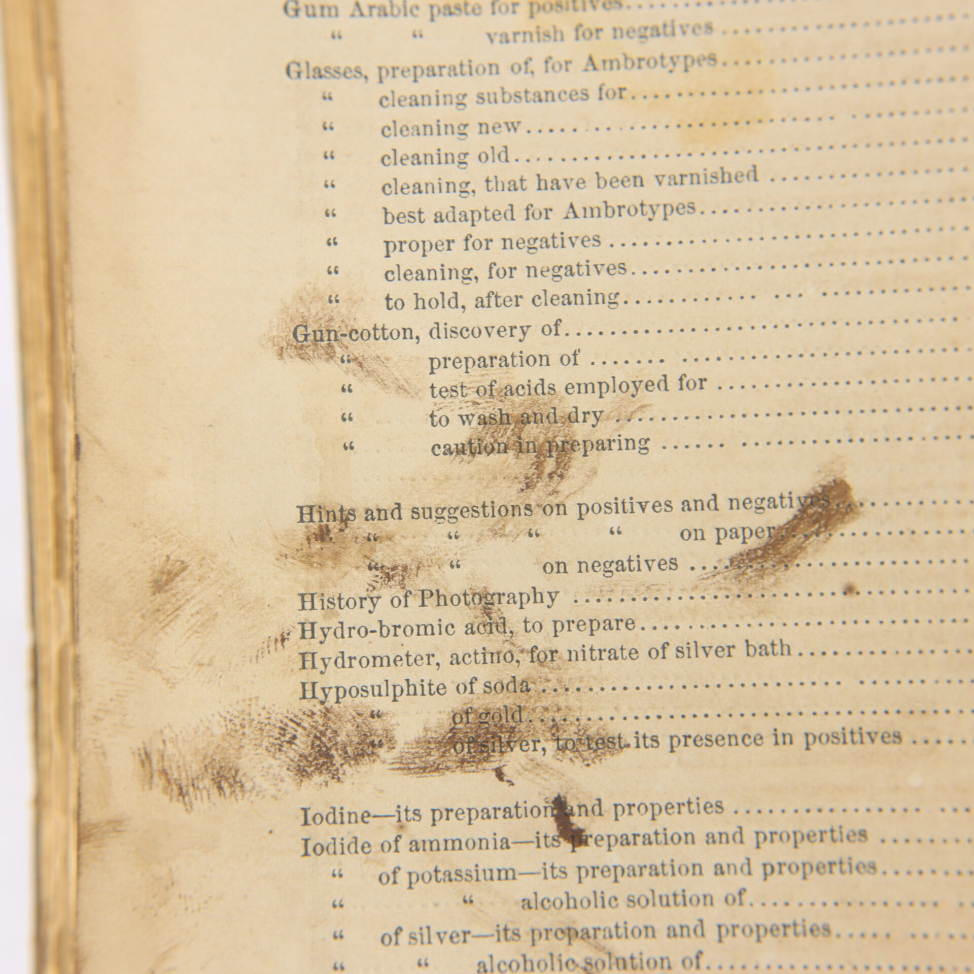 Close-up of a stained, aged book page showing a table of contents with topics related to photography, including chemicals and processes.