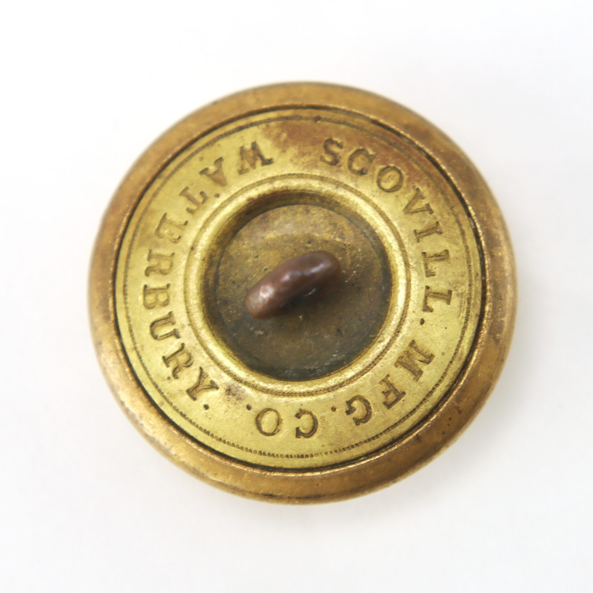 Round brass button with a central loop shank, engraved with the words "SCOVILL MF'G CO. WATERBURY" around the edge.