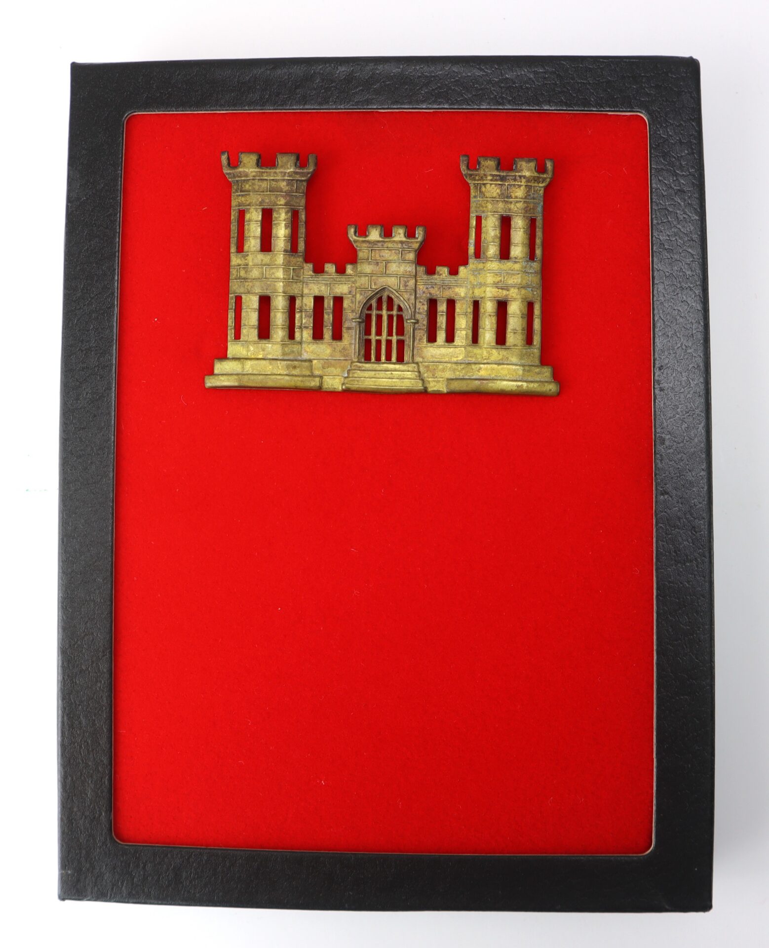 A gold castle insignia on a red background, framed in a black display case.
