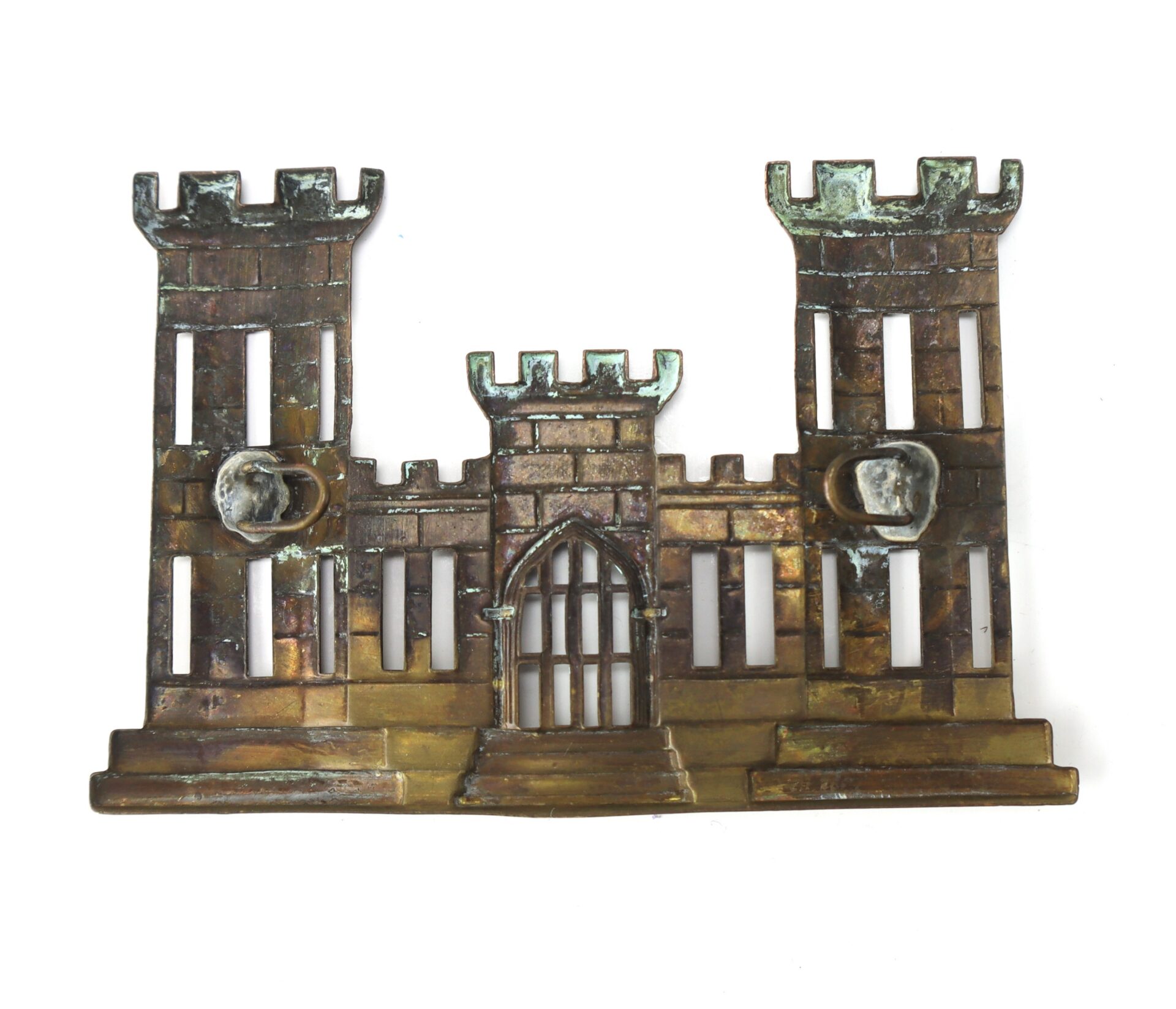 Bronze or brass wall plaque depicting a castle with two large towers, arched doorway, barred windows, and small animal head accents.