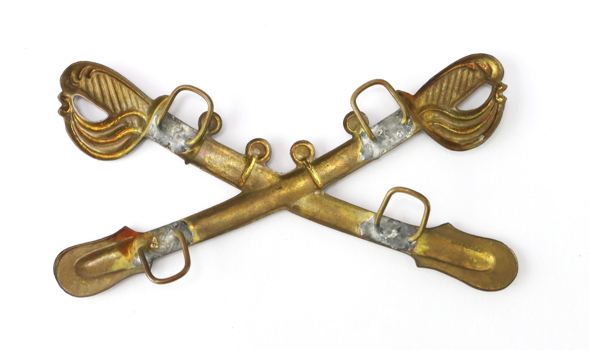 A brass crossed sabers military insignia with decorative hilts, typically used to represent cavalry units, shown on a white background.