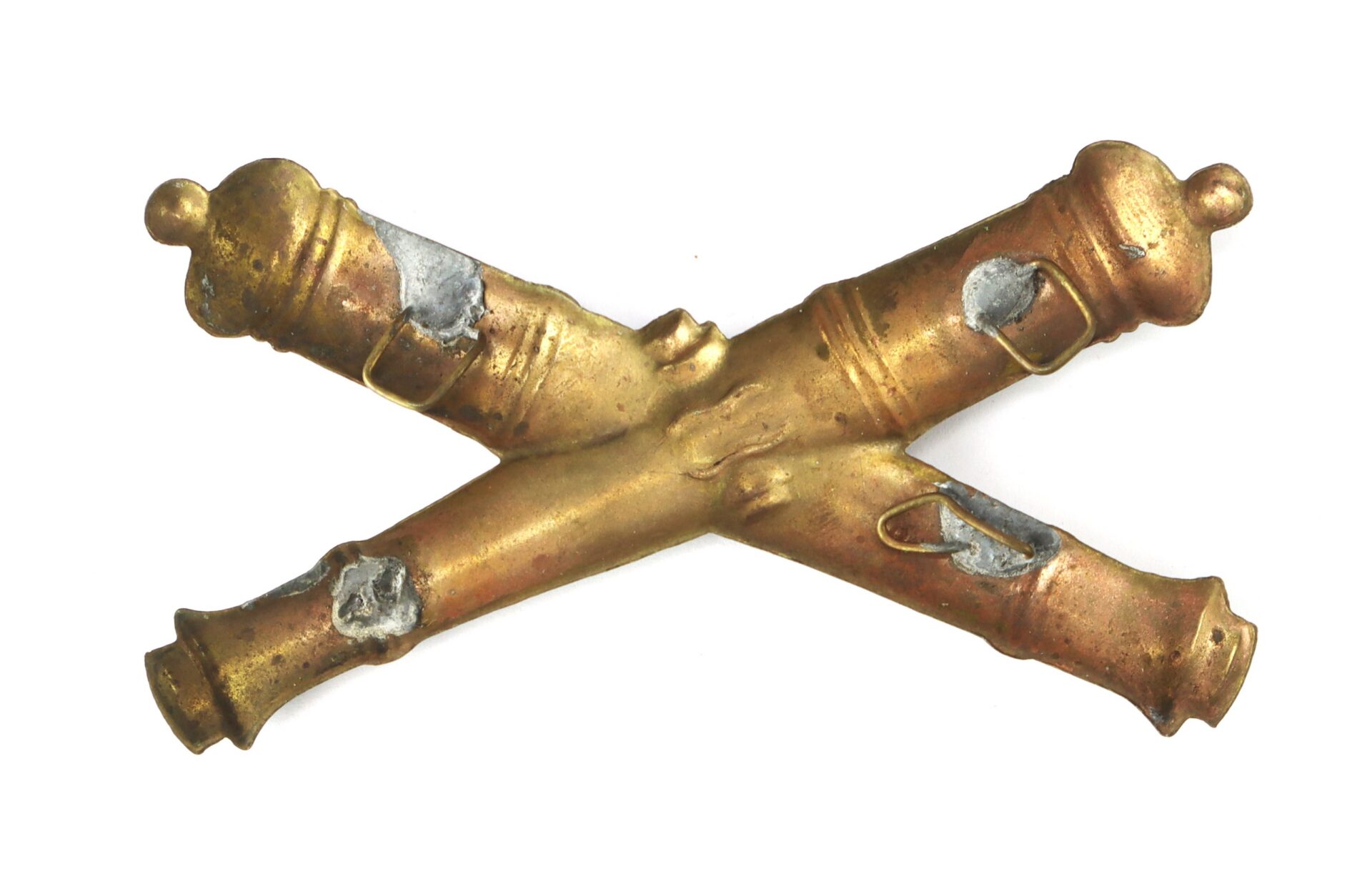 A brass insignia featuring two crossed cannons with visible wear and solder marks.