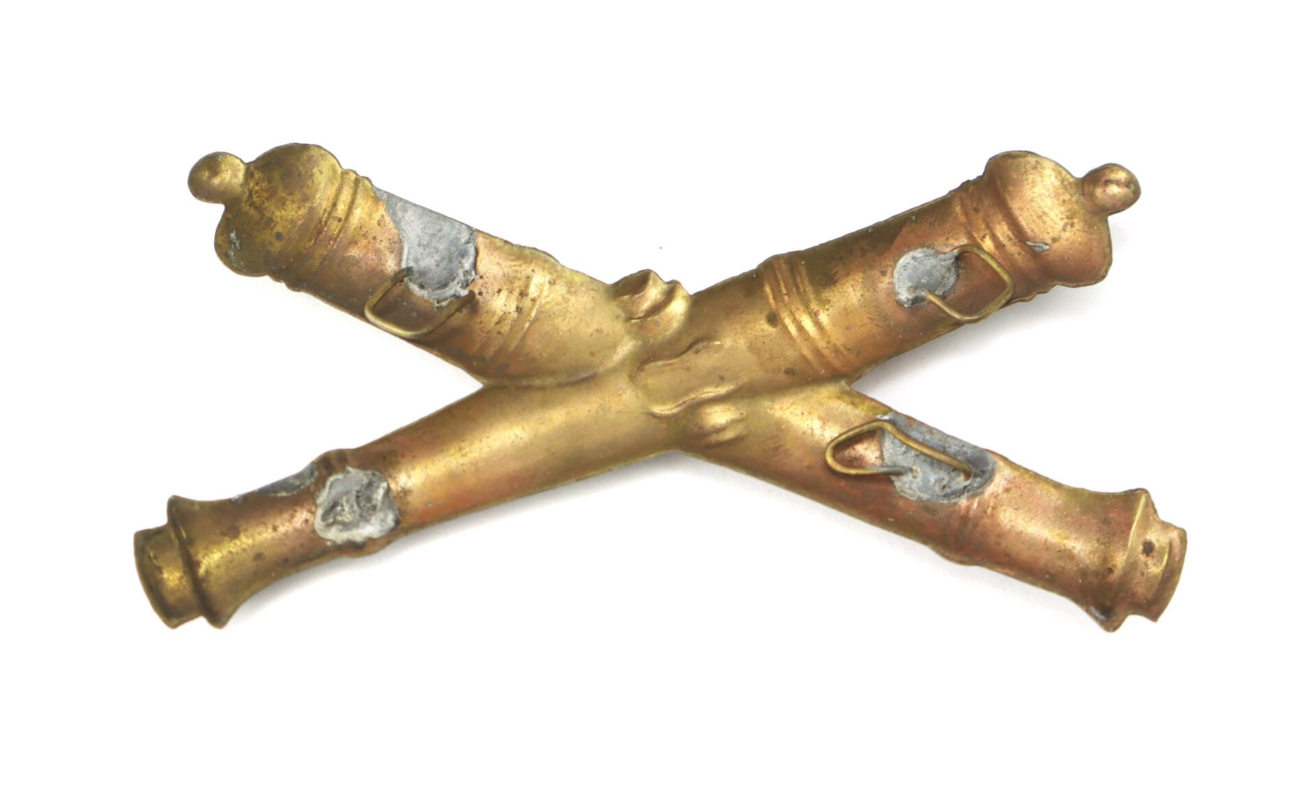 A brass insignia featuring two crossed cannons with visible wear and darkened spots.