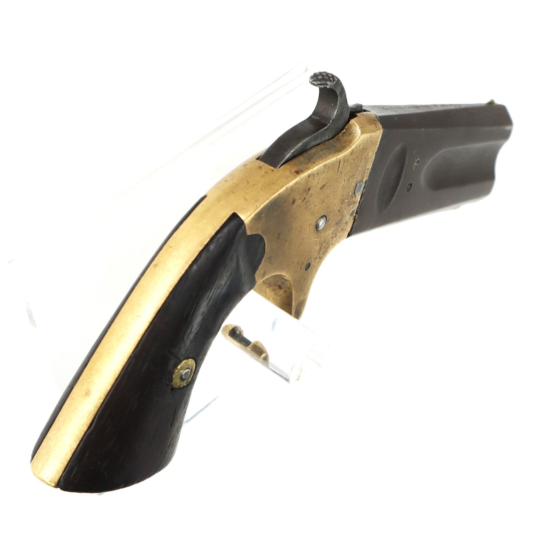 A small, antique, single-shot pistol with a brass frame, black grip, and raised hammer, displayed on a clear stand.