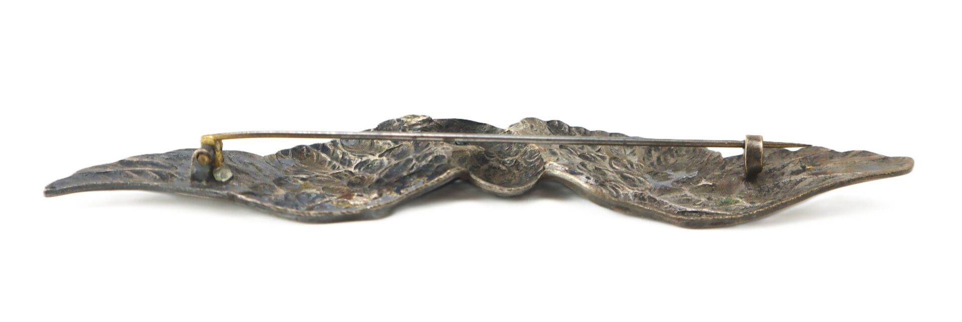 An antique metal brooch viewed from the back, showing a textured surface and a simple pin clasp mechanism.