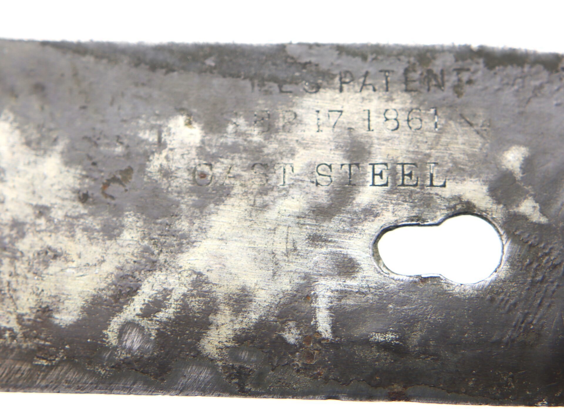 Close-up of a worn metal blade showing engraved text with the words "PATENT," "APR 17 1861," and "CAST STEEL," along with a keyhole-shaped slot.