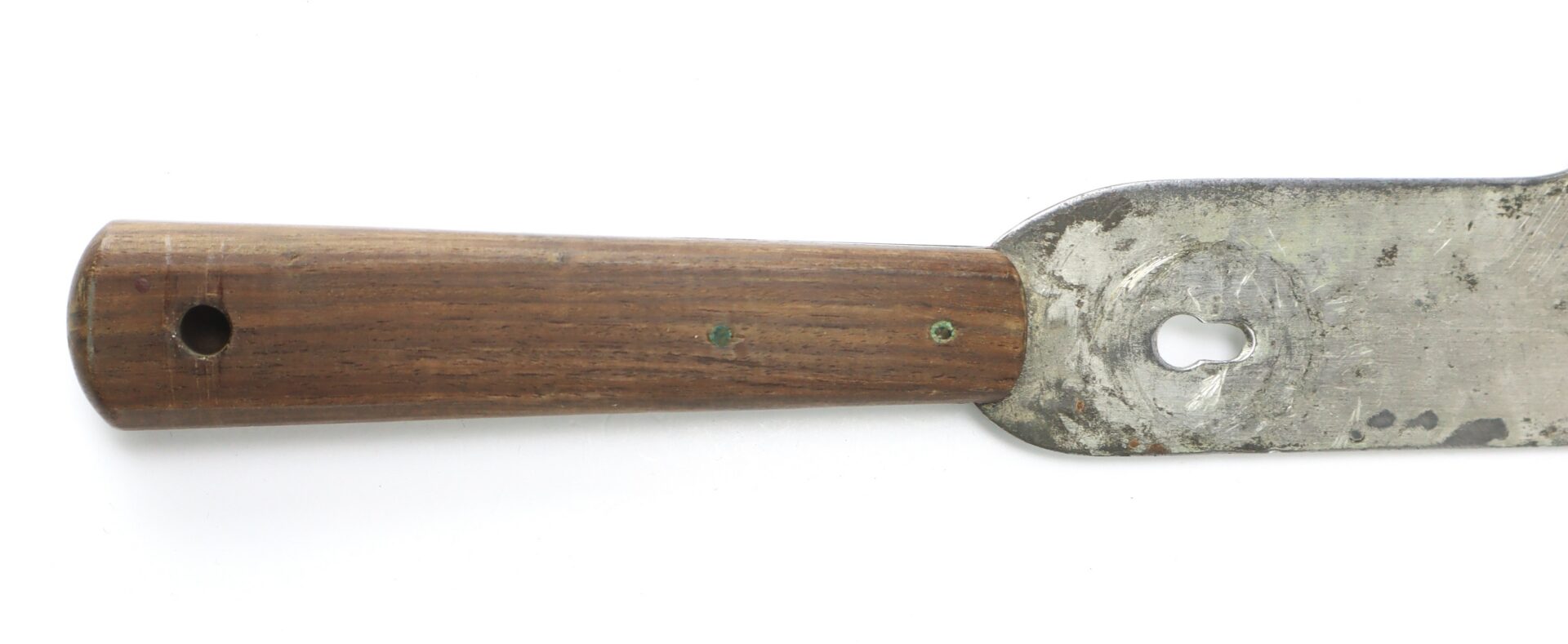 A close-up of a metal spatula with a wooden handle, showing signs of wear and a hole near the base of the blade.