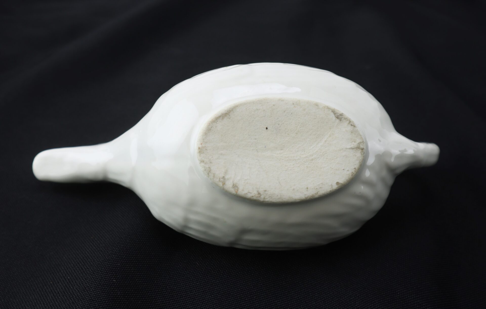 A white ceramic object with an oval base and a narrow handle, shown upside down on a black background.