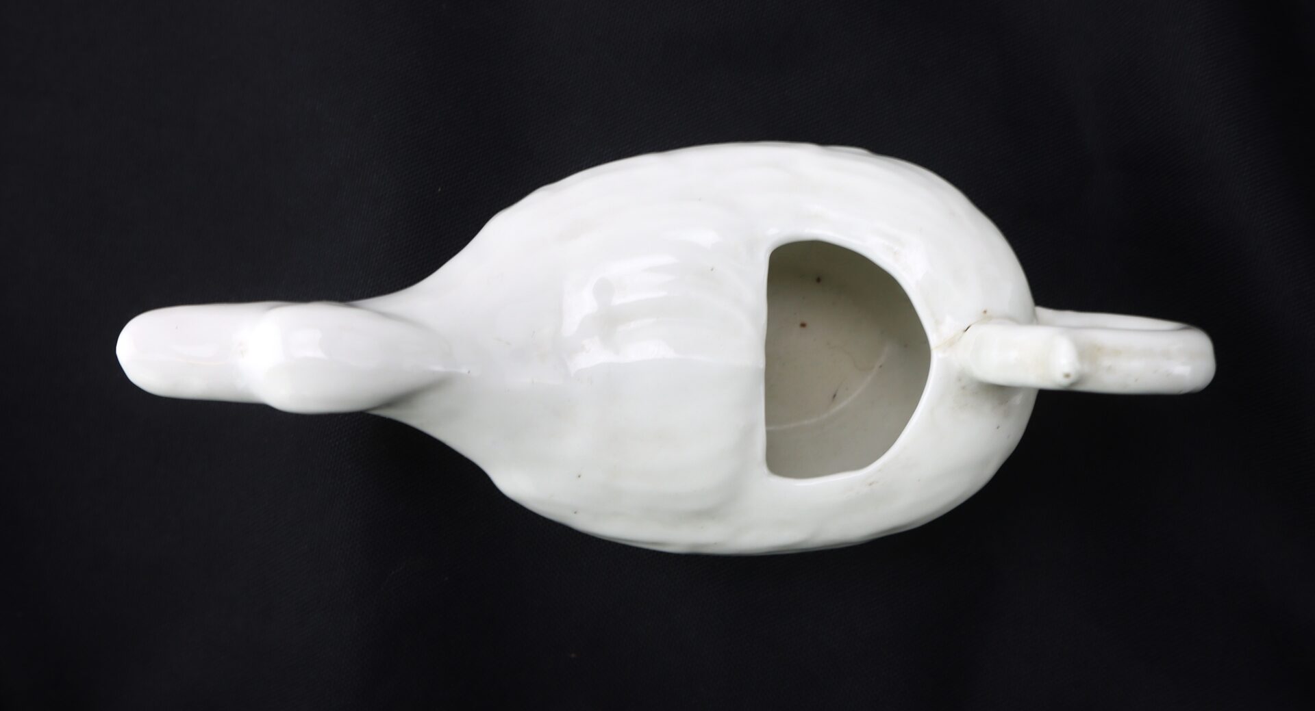 White ceramic object with two handles and a large cutout on top, placed on a black background.