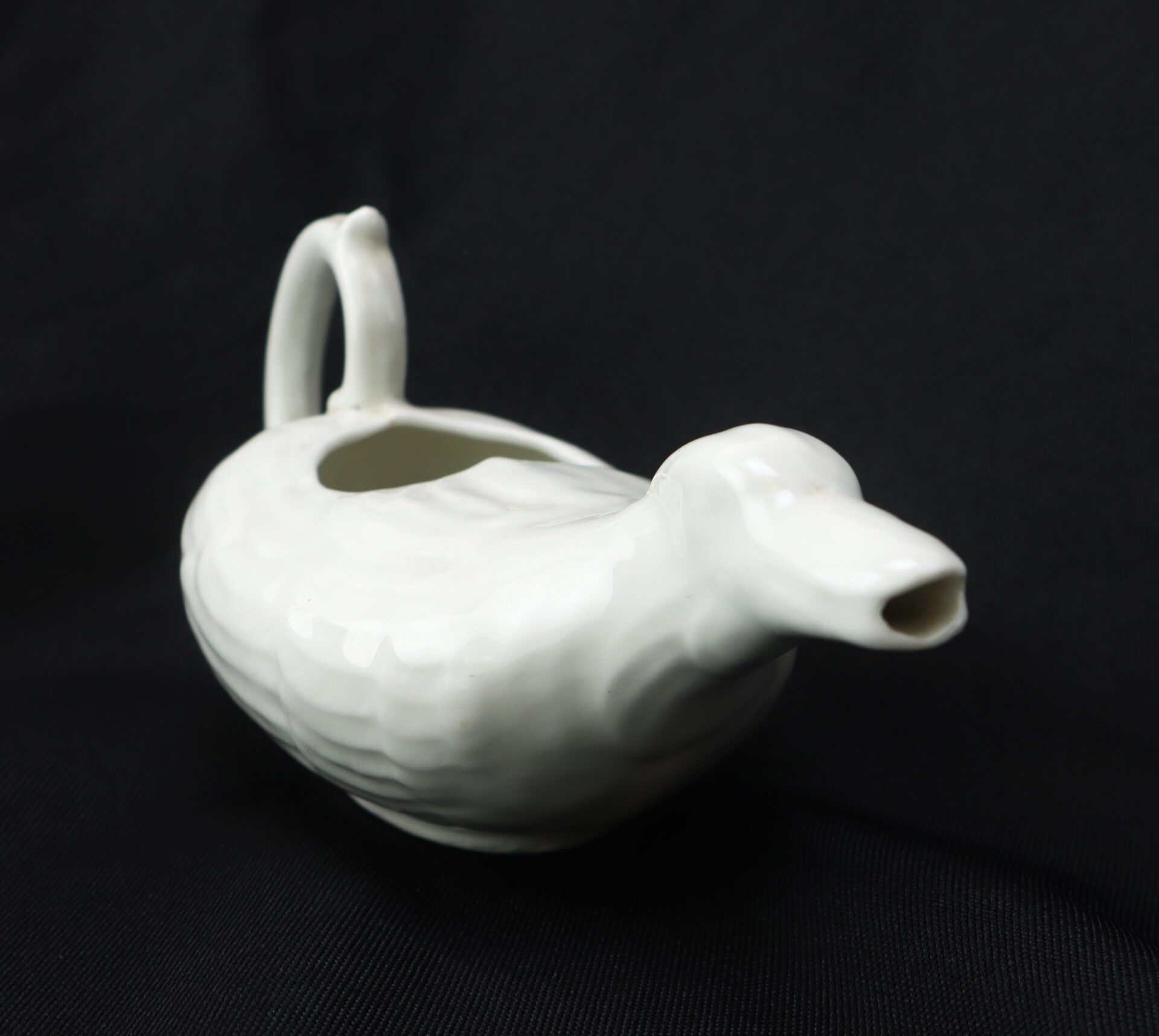 White ceramic gravy boat shaped like a duck, shown on a black background.