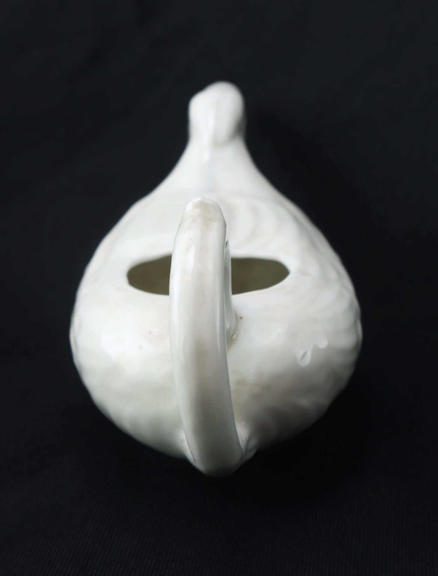 White ceramic teapot with a handle and spout, viewed from above against a black background.