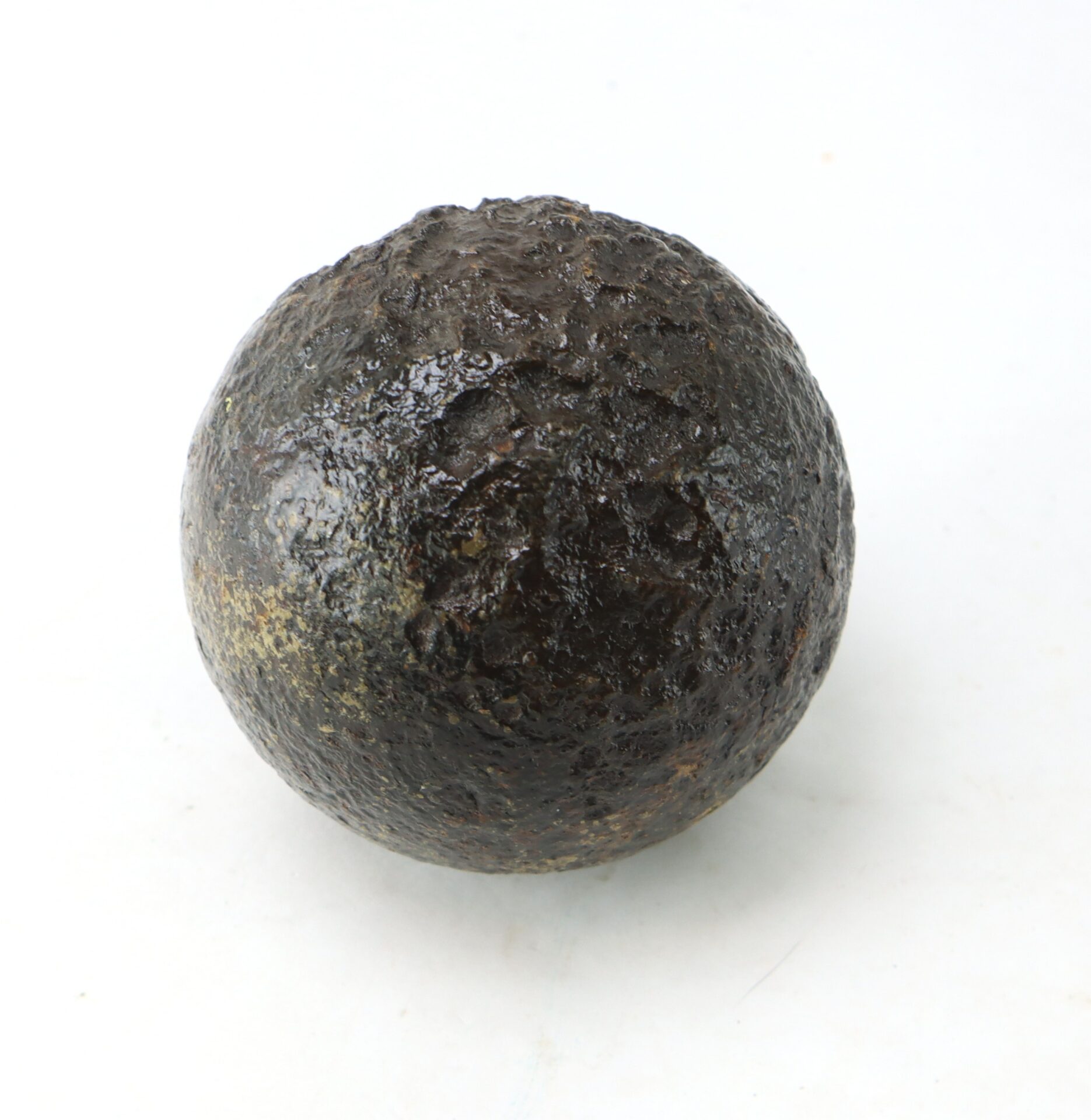 A dark, rough-textured metal cannonball is shown on a plain white background.