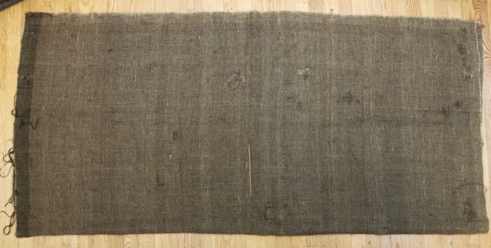 A rectangular piece of coarse, brown burlap fabric with visible wear and frayed edges, laid flat on a wooden floor.