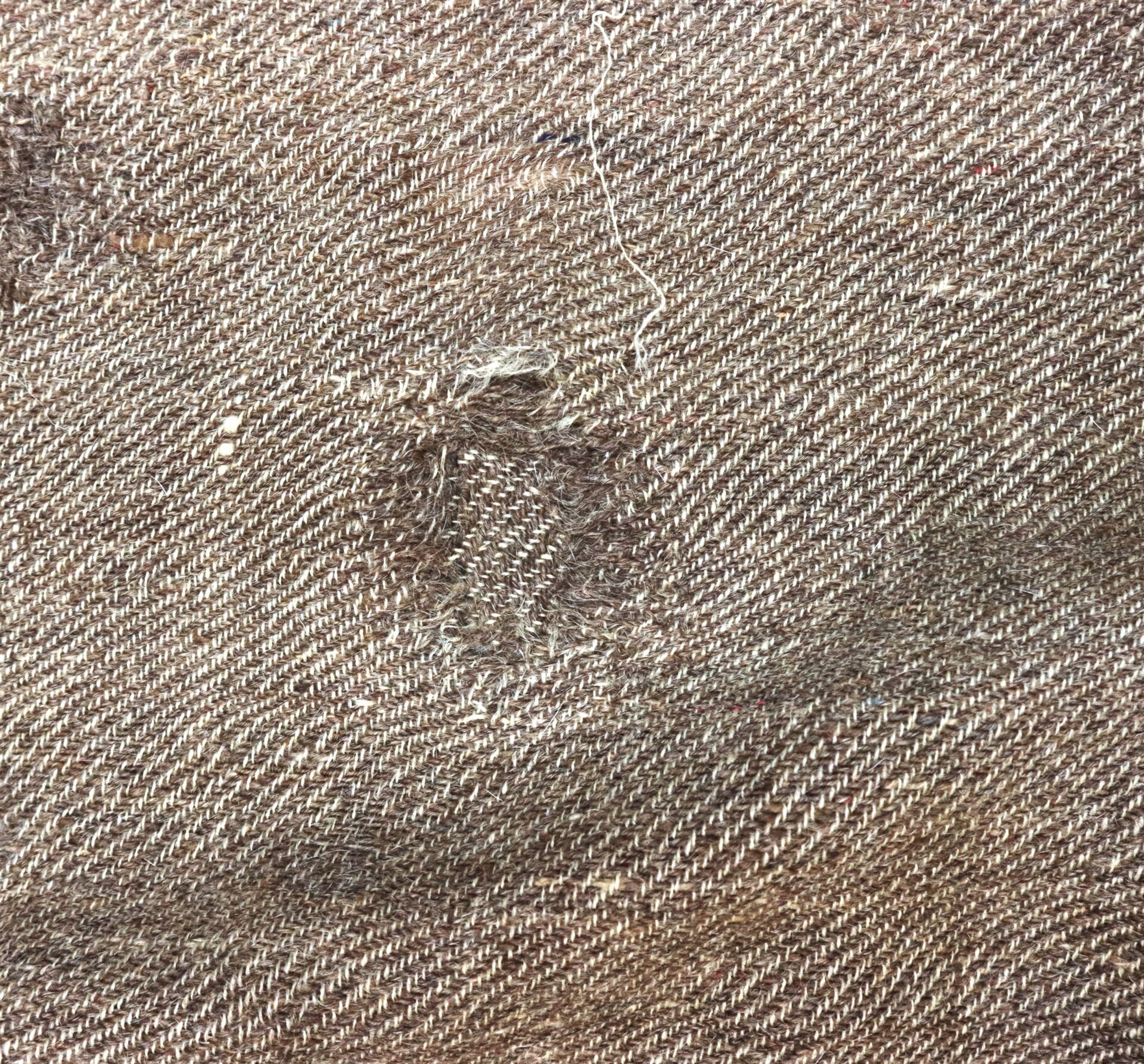 Close-up of brown woven fabric with a rectangular patch where the material has been visibly repaired.