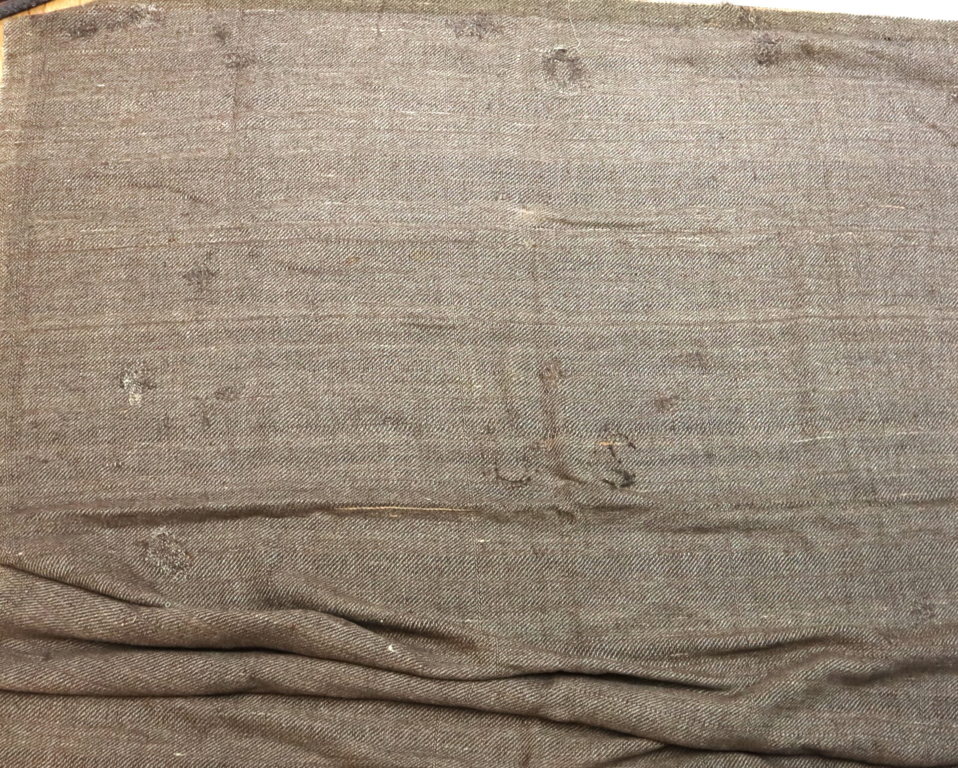 A piece of brown fabric with visible wear, scattered small holes, and some creases near the bottom.