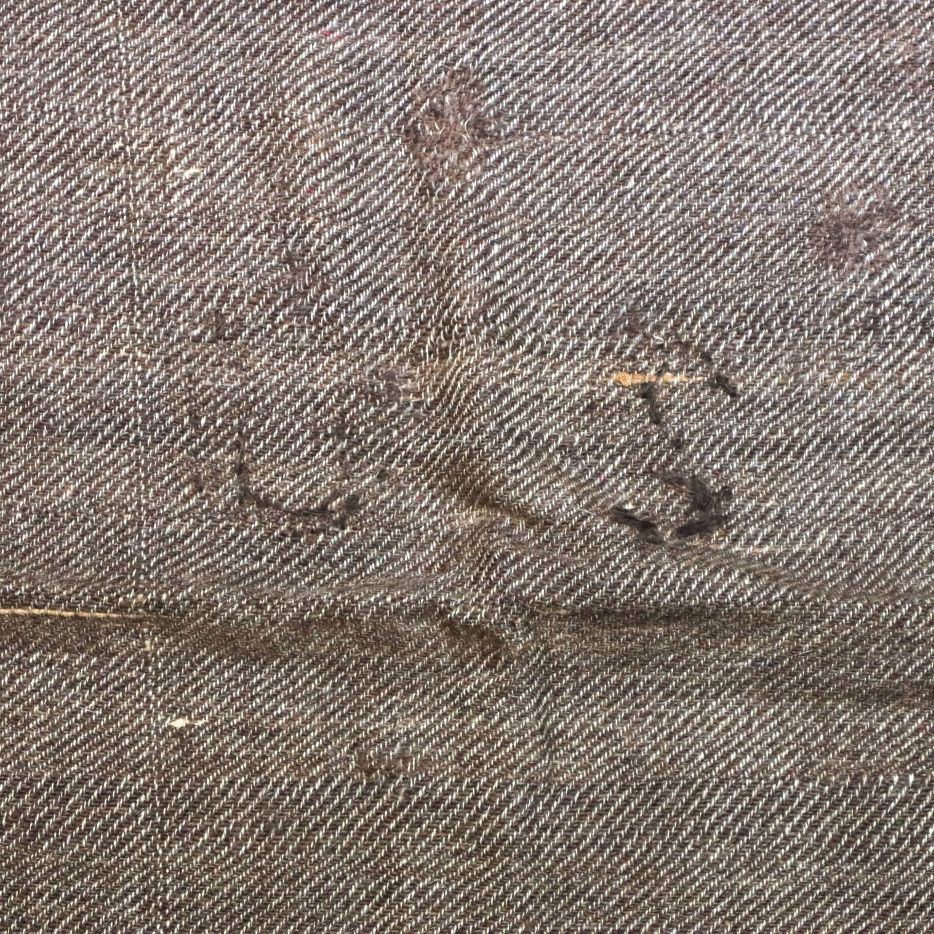 Close-up of a brown, textured fabric with visible seams, creases, and some dark stains scattered across the surface.