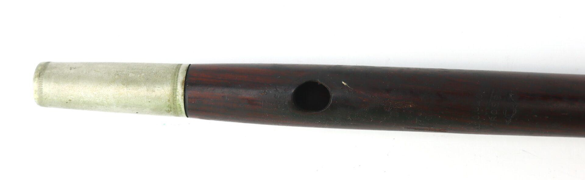 Close-up of a woodwind musical instrument, showing a dark wooden body with a single tone hole and a metal mouthpiece fitting.