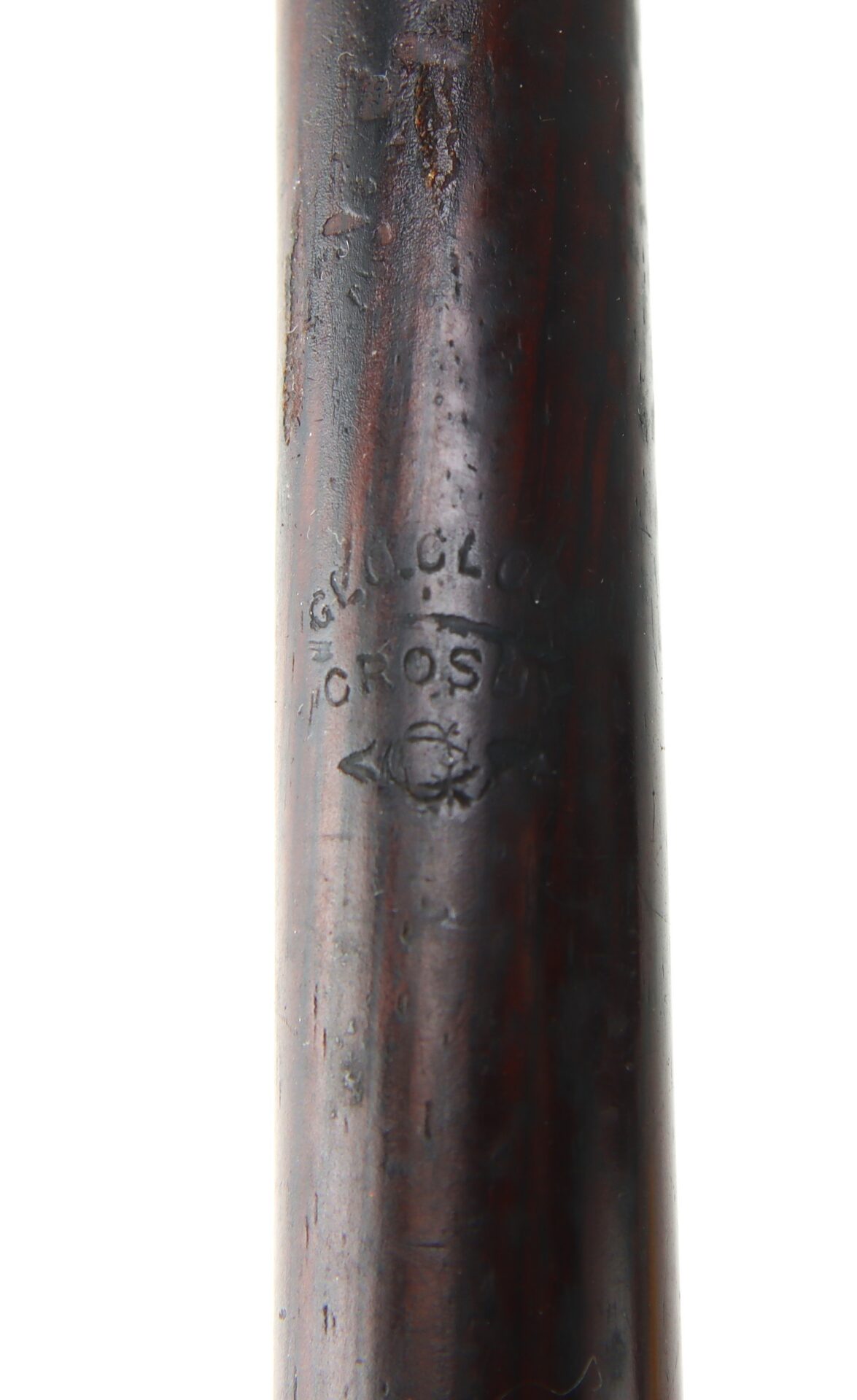 Close-up of a dark wooden cylindrical object with a partially visible engraved stamp reading “CROSLY” and decorative details.