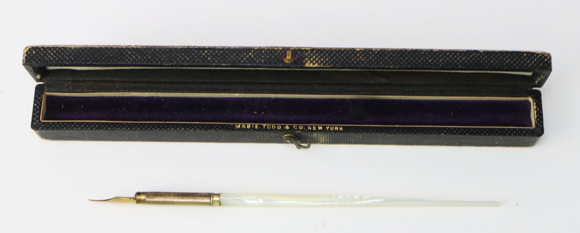 A vintage dip pen with a mother-of-pearl handle and metal nib, displayed in an open black case lined with purple velvet.
