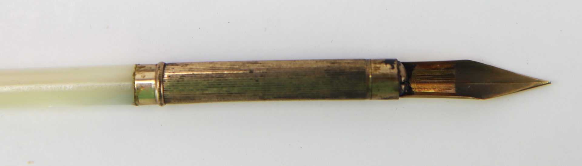 A close-up of a vintage metal dip pen with a gold-colored nib and an ivory-colored handle on a white background.