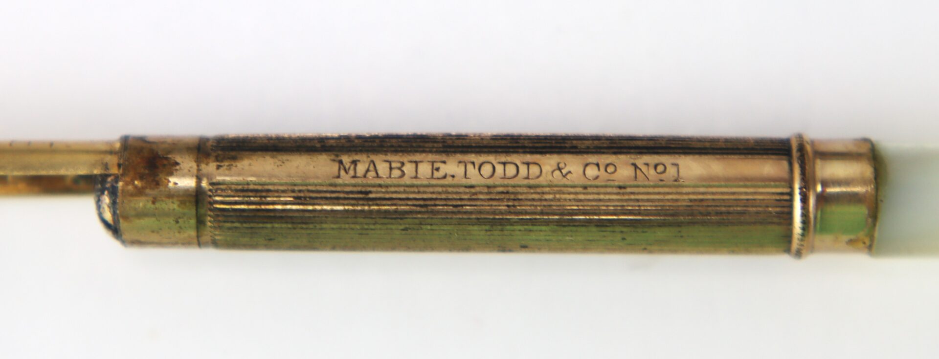 Close-up of a vintage pen barrel with the engraving "MABIE, TODD & CO No1" on a gold-colored metal surface.