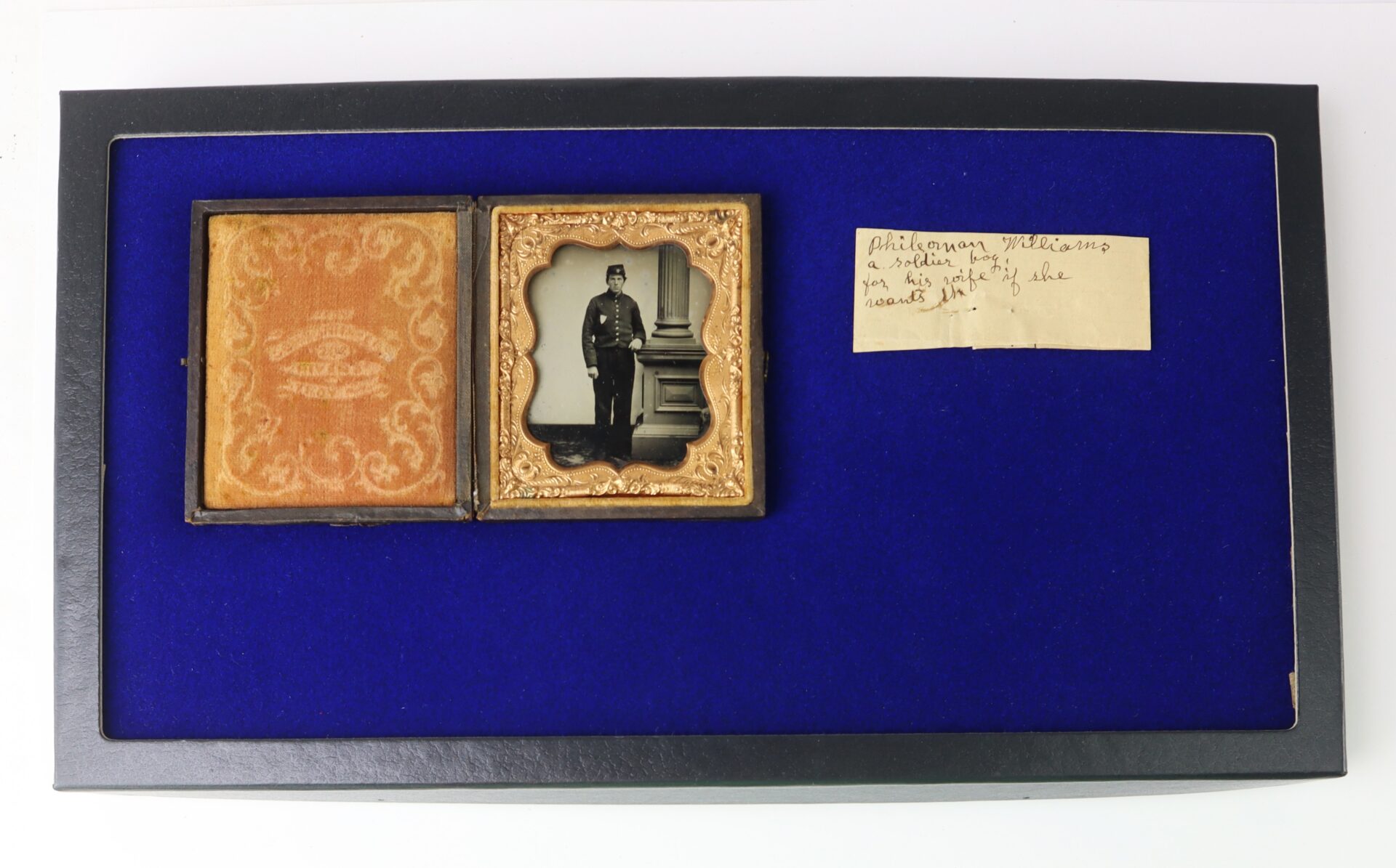A framed display with an old photograph of a man in a decorative case, a blue background, and a handwritten label identifying the subject.