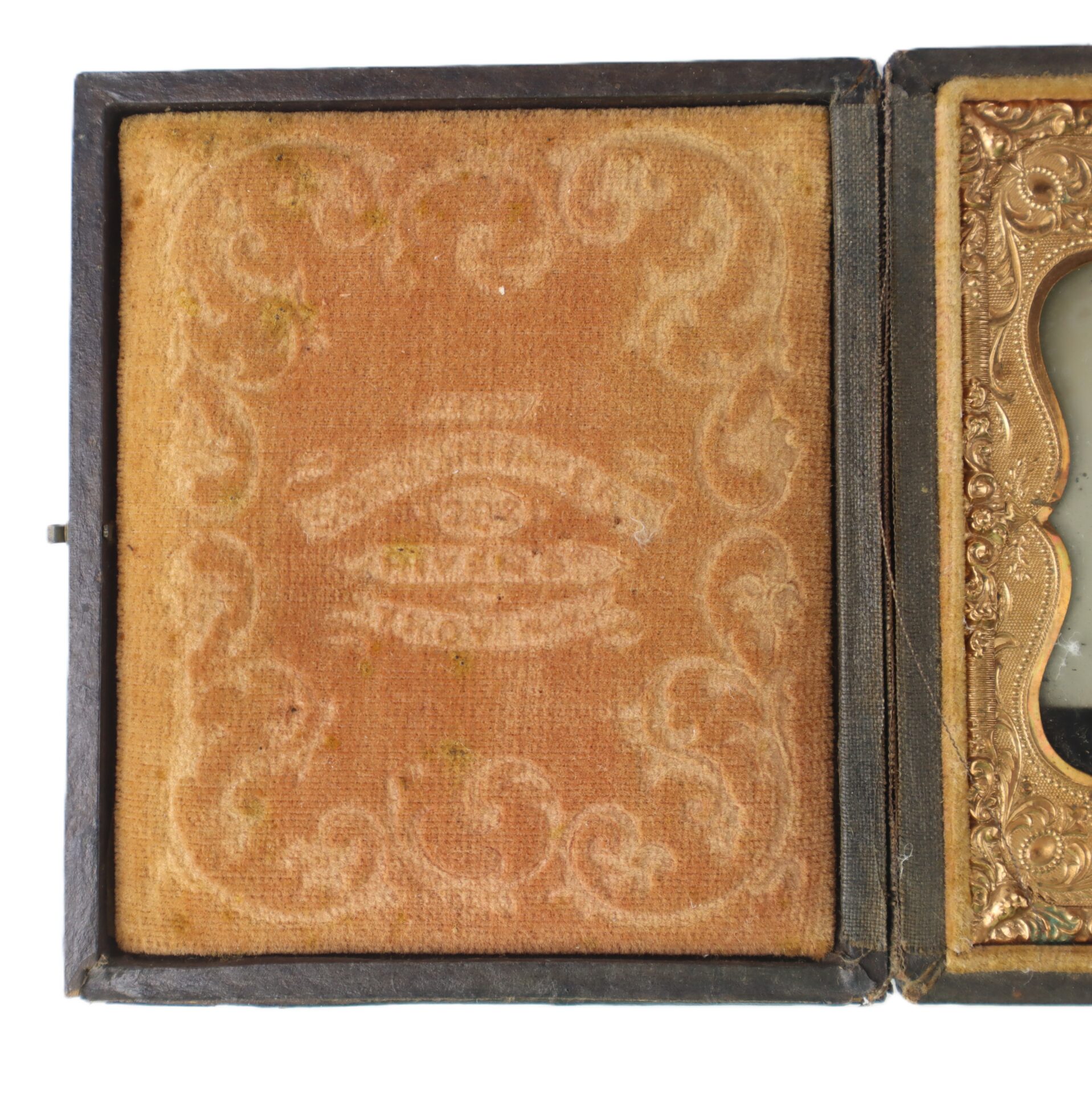 A vintage case lined with faded, patterned fabric featuring a faint embossed eye design and decorative swirls, partially open to reveal a gilt-edged interior.