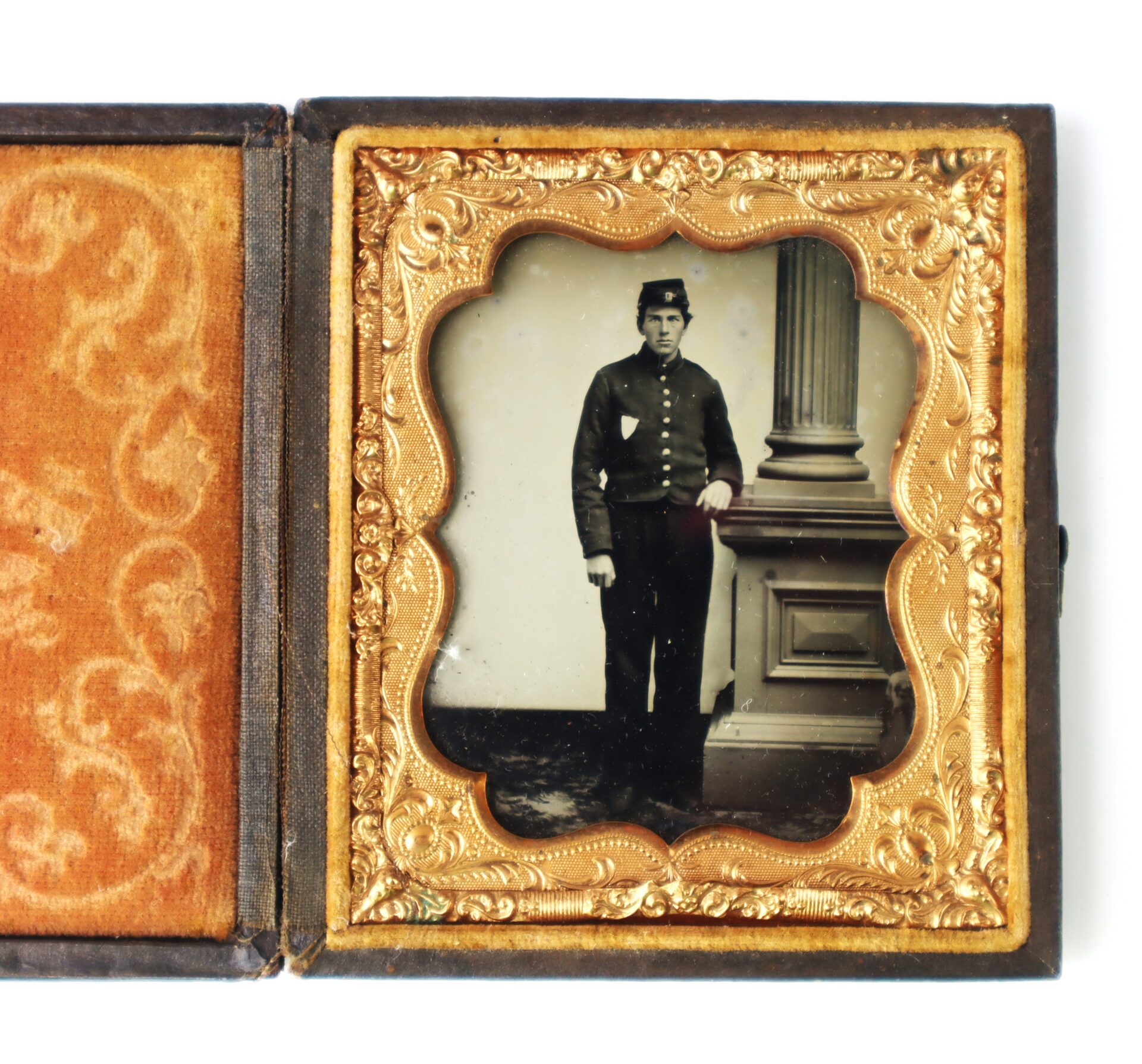 A vintage photograph of a man in a Civil War-era military uniform standing beside a column, framed in an ornate gold case.