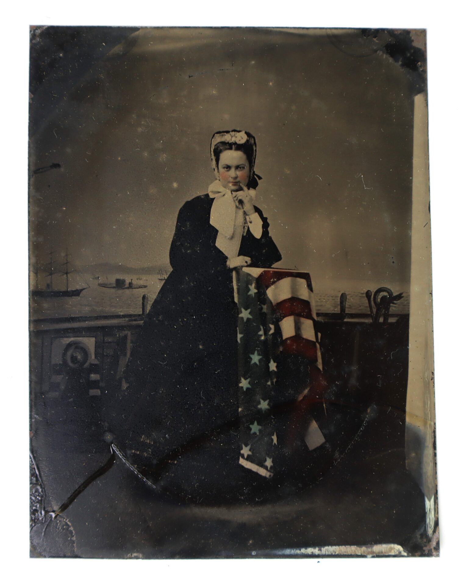 A woman in 19th-century clothing stands on a ship deck holding an American flag, with sailing ships and water visible in the background.