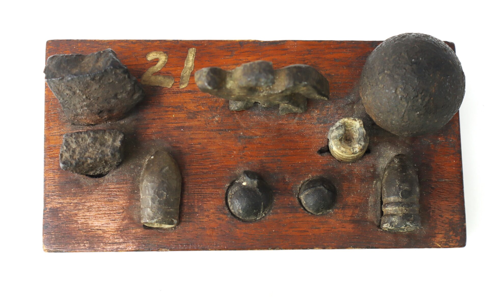 A wooden display board holds various old metal ammunition pieces, including bullets, a musket ball, and other projectile fragments, with the number 21 marked on the board.