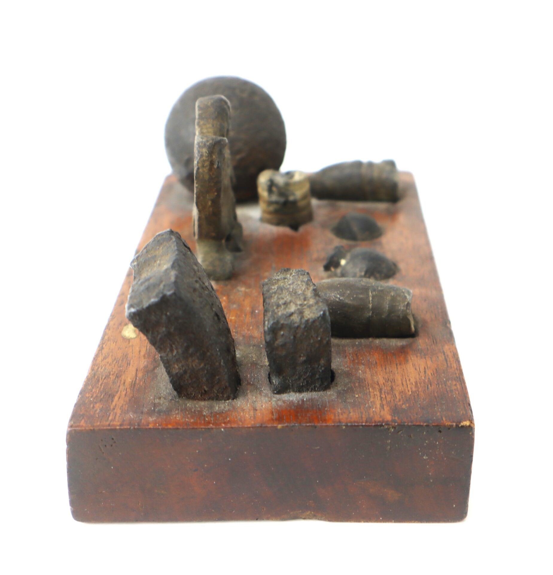 A wooden display block with embedded antique lead bullets, fragments, and a round musket ball, viewed from a low front angle.