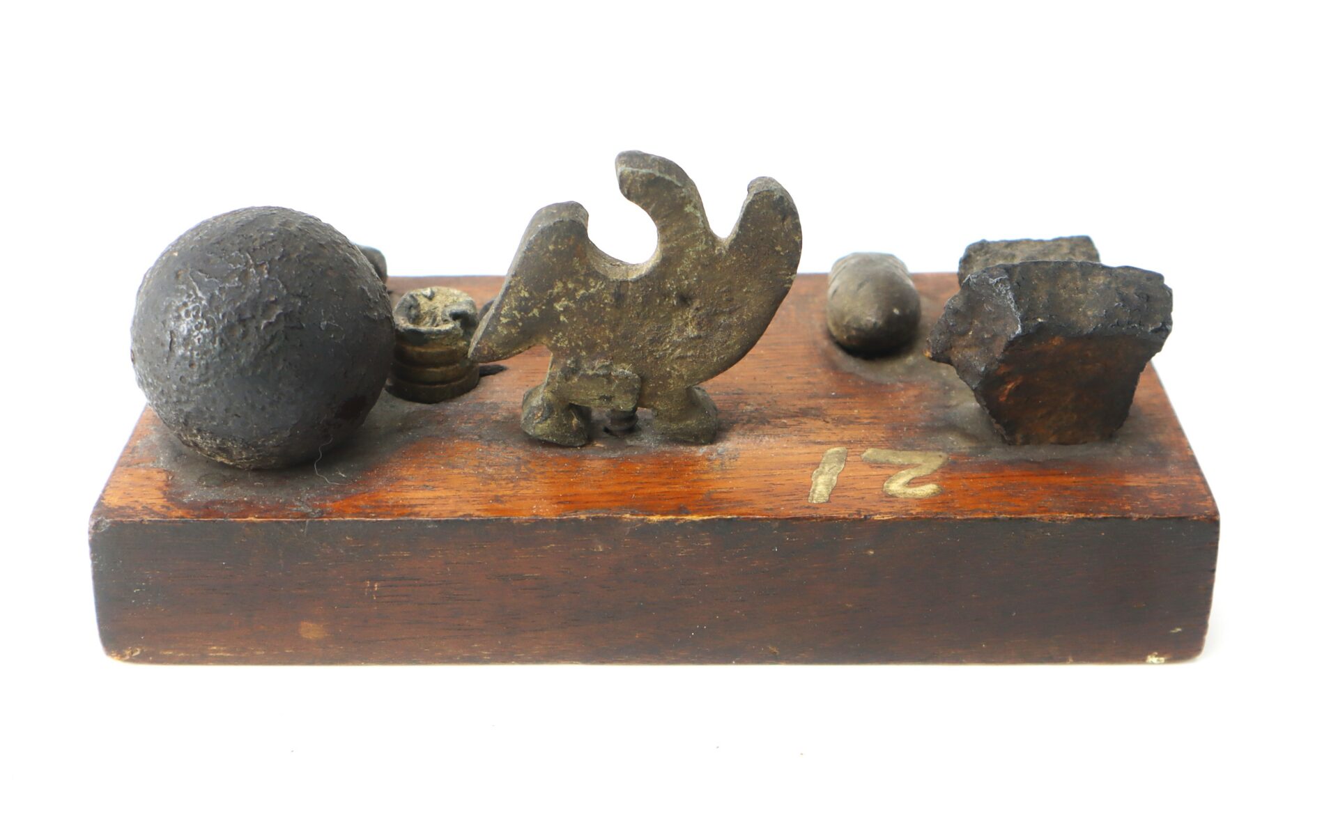 A wooden base displaying various old metal weights in different shapes, including a sphere, a bird figure, a cube, and smaller irregular forms.