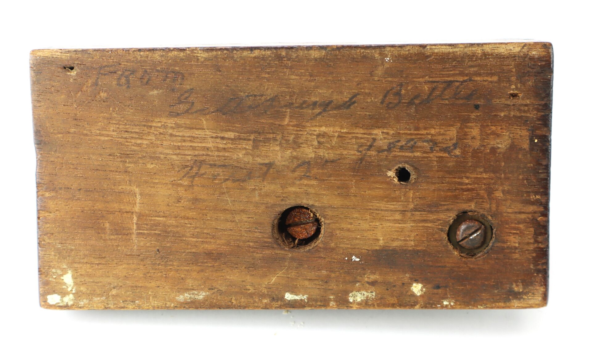 Rectangular piece of aged wood with handwritten text, one rusted screw, one regular screw, and a small drilled hole.