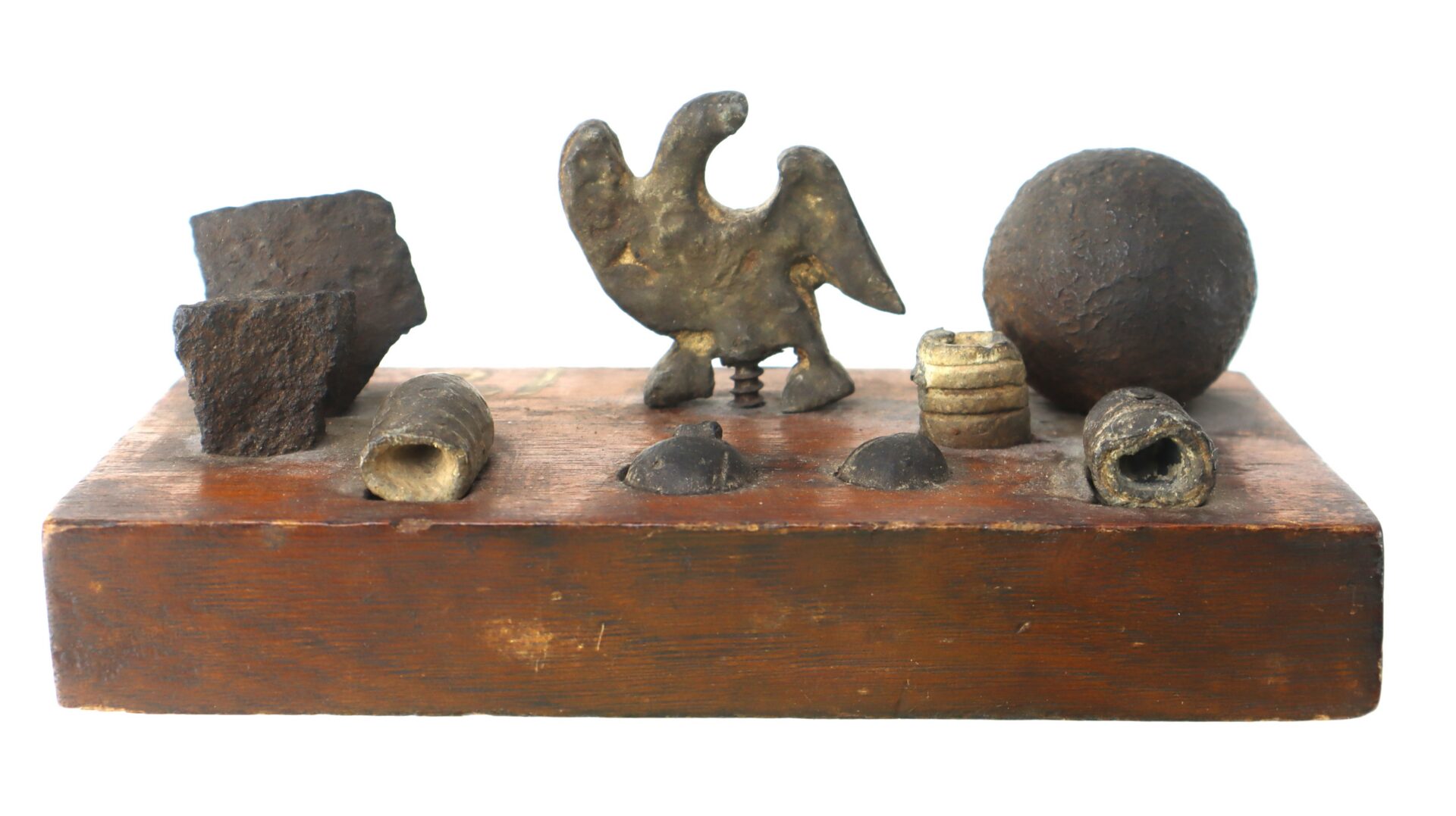 A wooden display holds various Civil War relics, including an eagle figurine, a cannonball, bullets, and metal fragments, all arranged on a rectangular base.