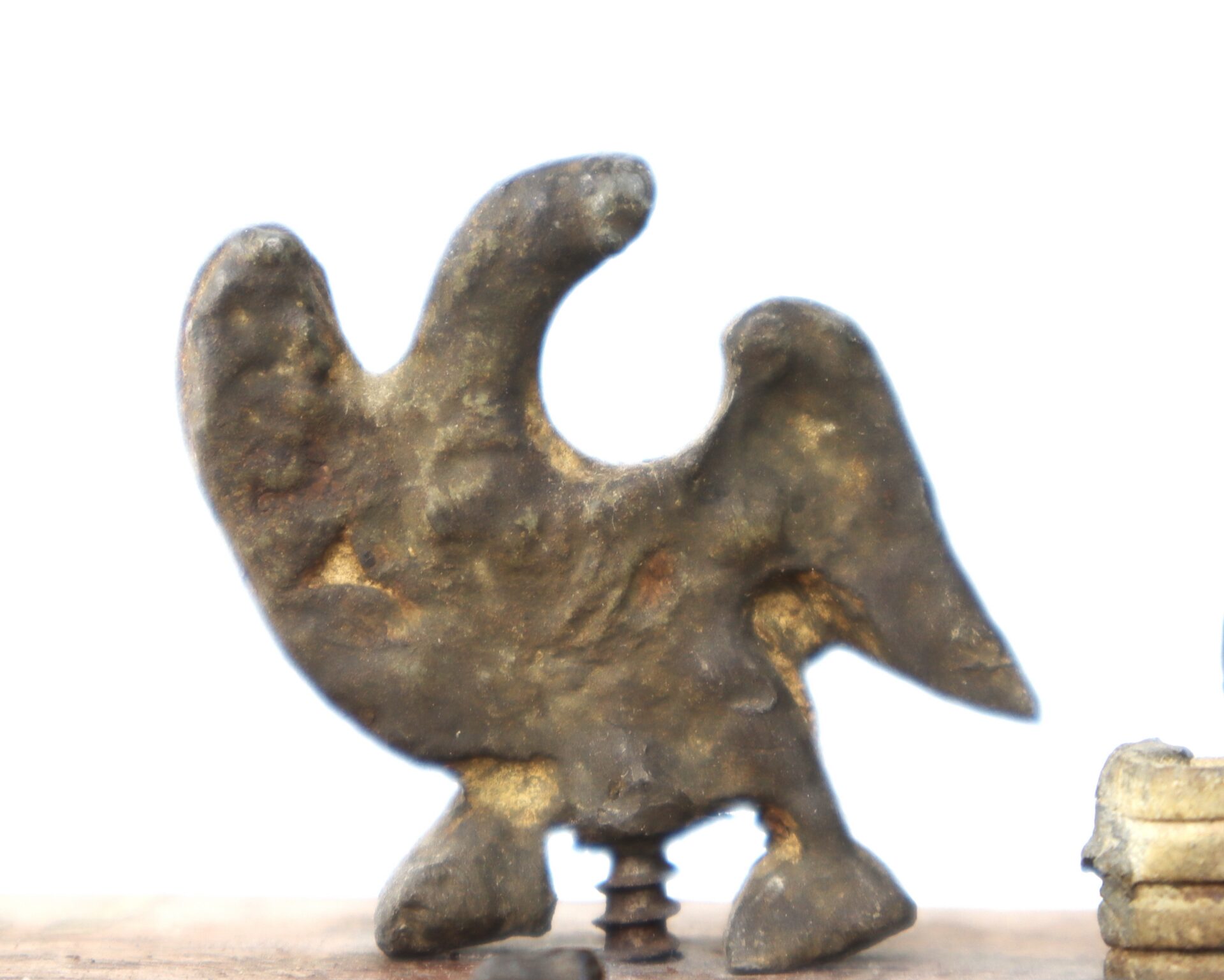 A rough, bird-shaped metal object with wings and legs, mounted on a screw, set against a plain white background.