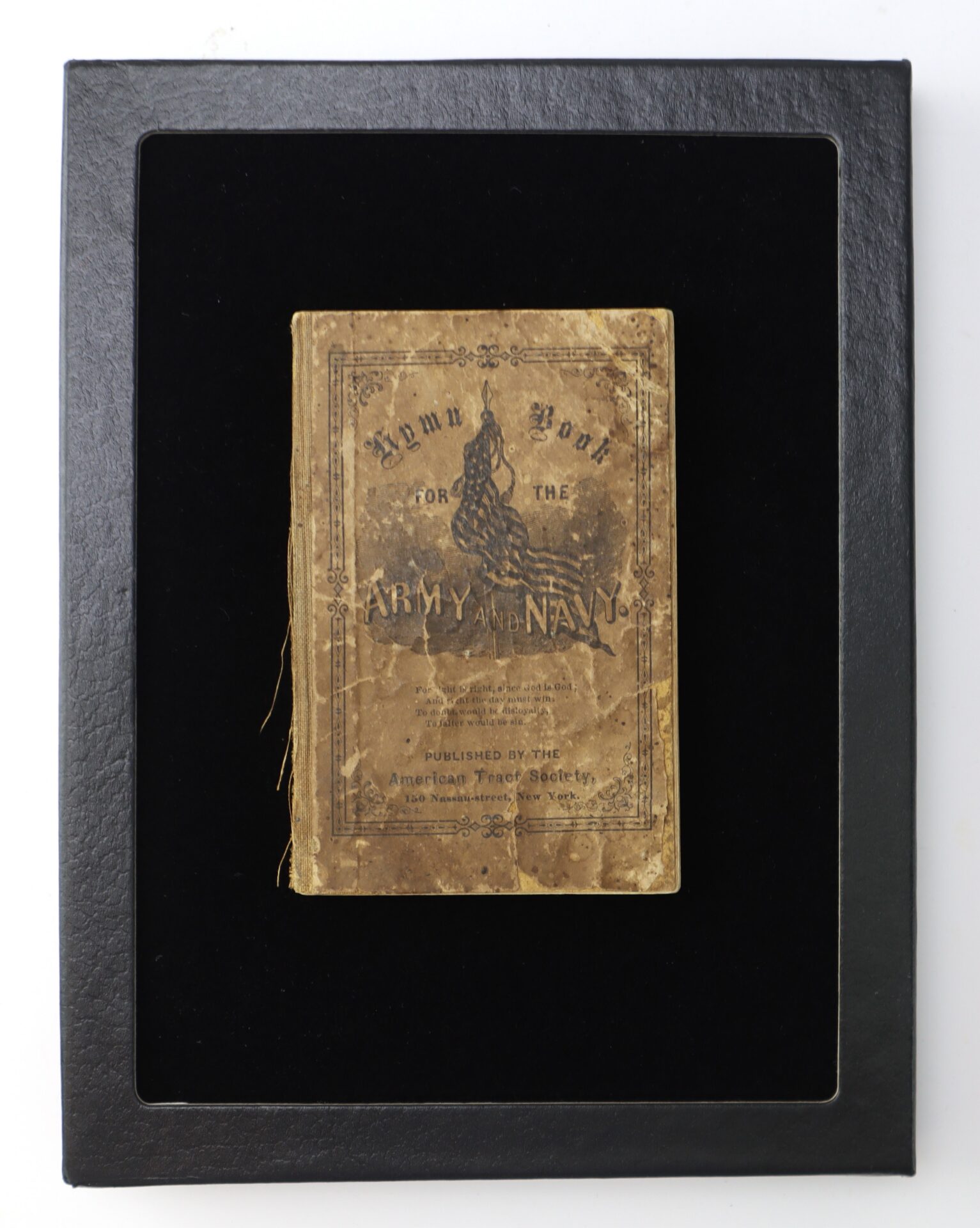 A worn "Hymn Book for the Army and Navy" with a faded cover is displayed in a black frame against a black background.