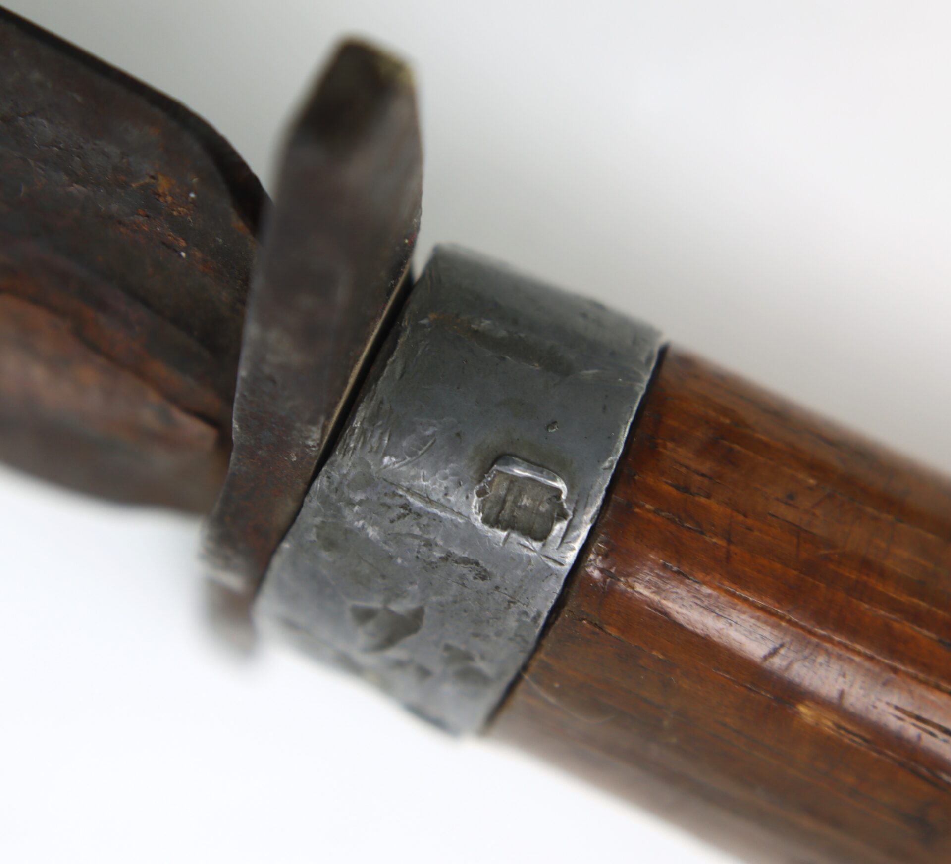 Close-up of a metal band securing a rusty blade to a wooden handle, with visible wear and scratches on the surfaces.