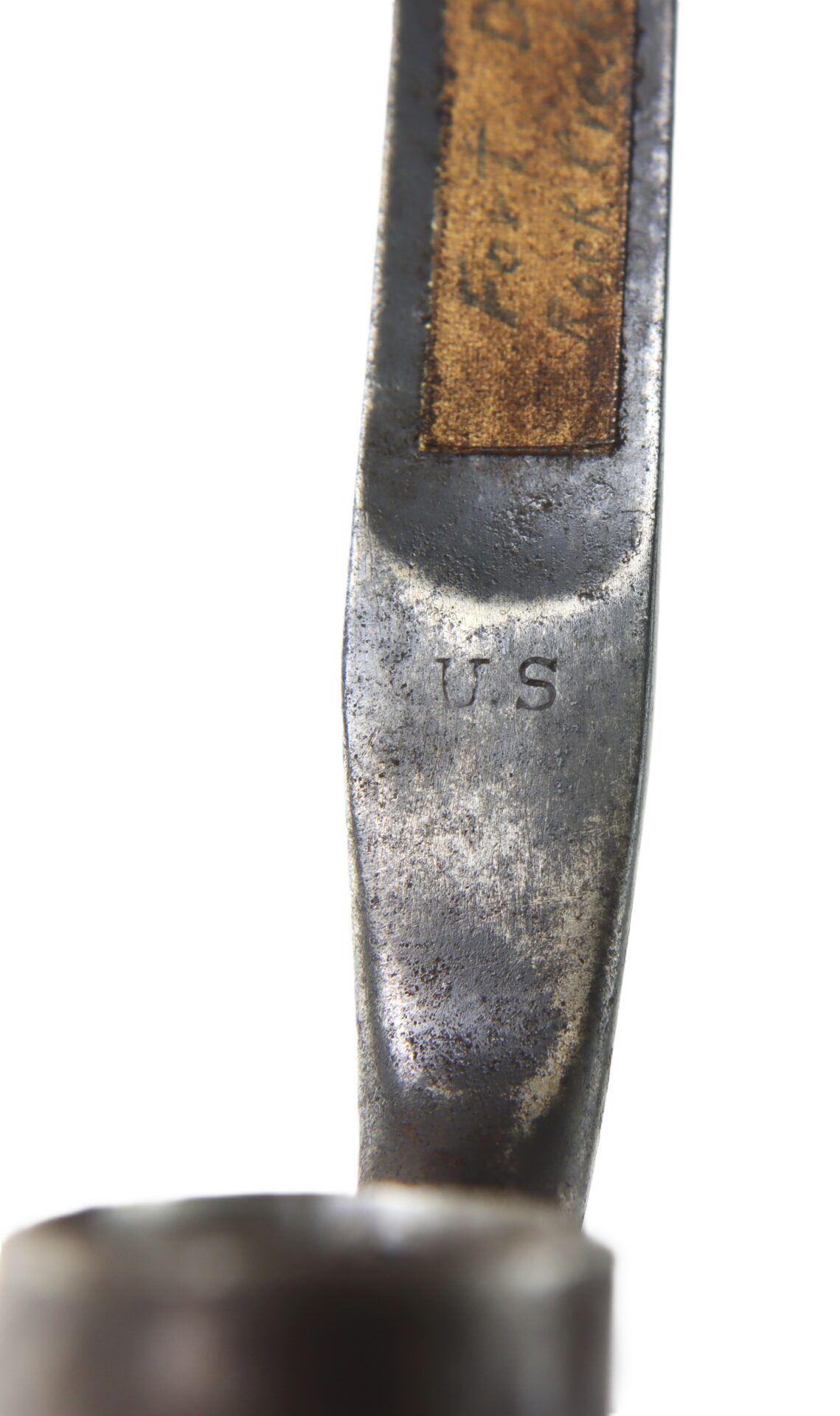 Close-up of a metal object with a worn surface, featuring the engraved letters "U S" and a section with a brown strip, possibly leather or wood.