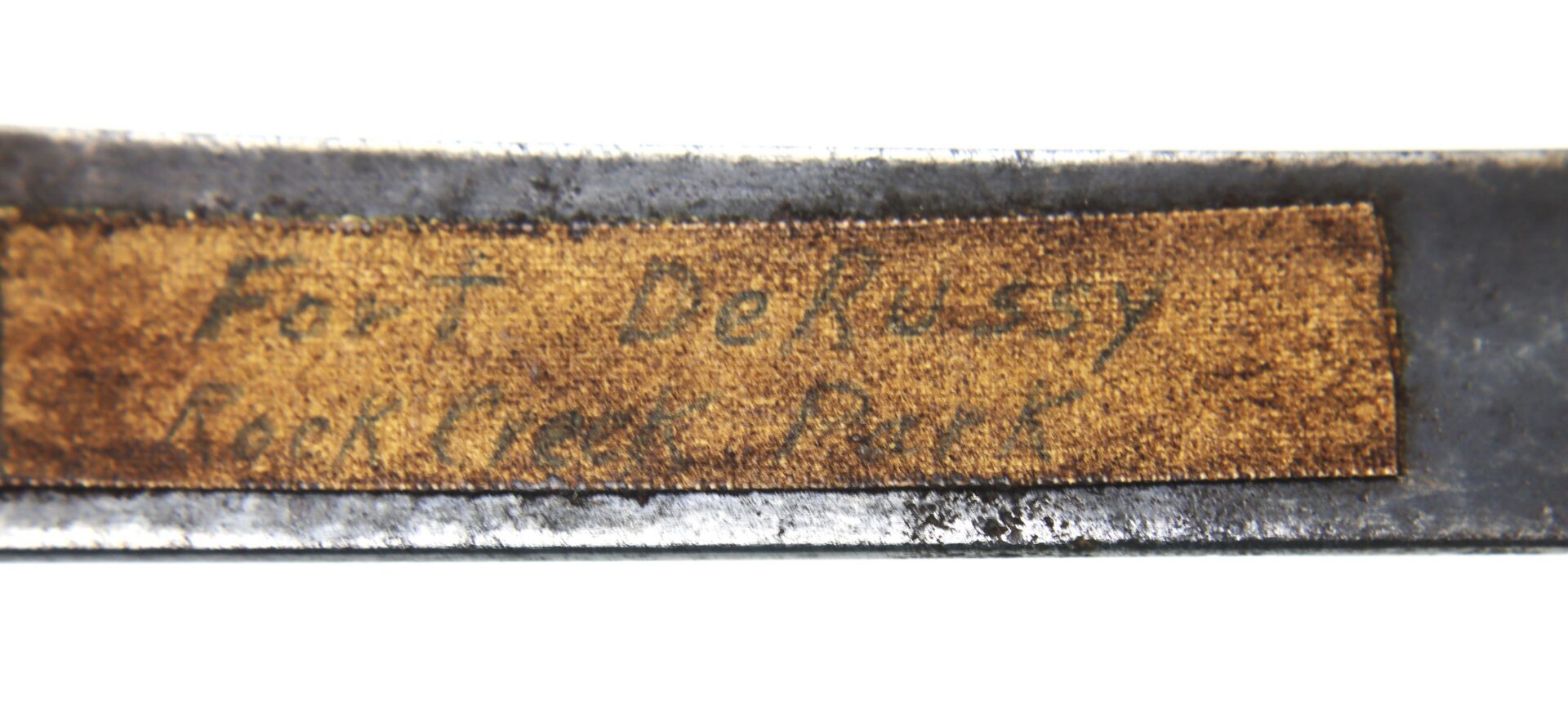 Close-up of a metal object with a worn label that reads "Fort De Russy Rock Core - Bore" in faded handwriting.