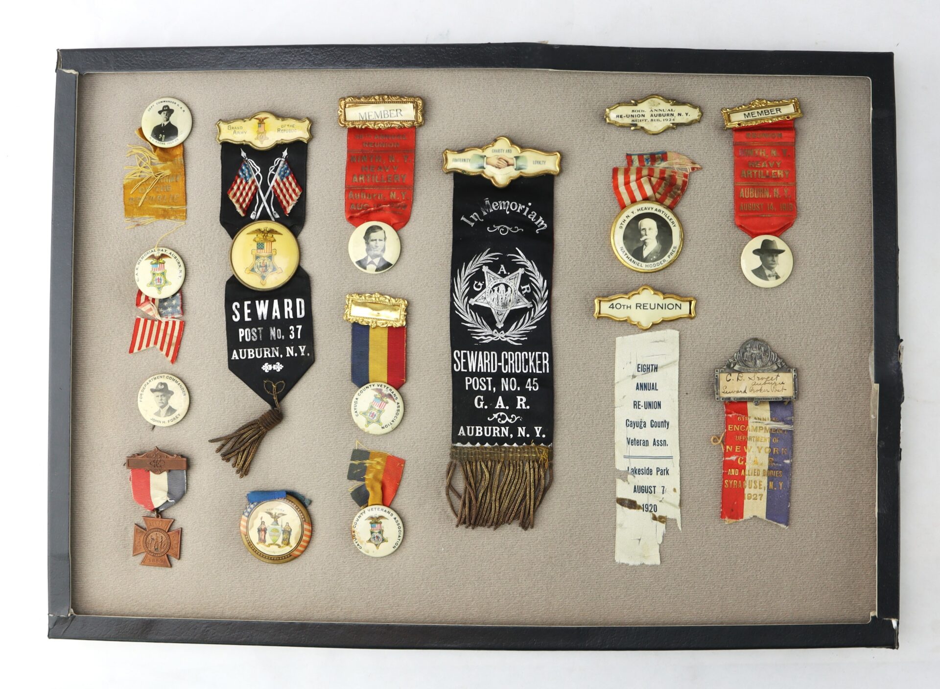 A display case containing various vintage medals, ribbons, and pins from Seward Post No. 37 and No. 45, G.A.R., Auburn, N.Y., with portraits and American patriotic designs.
